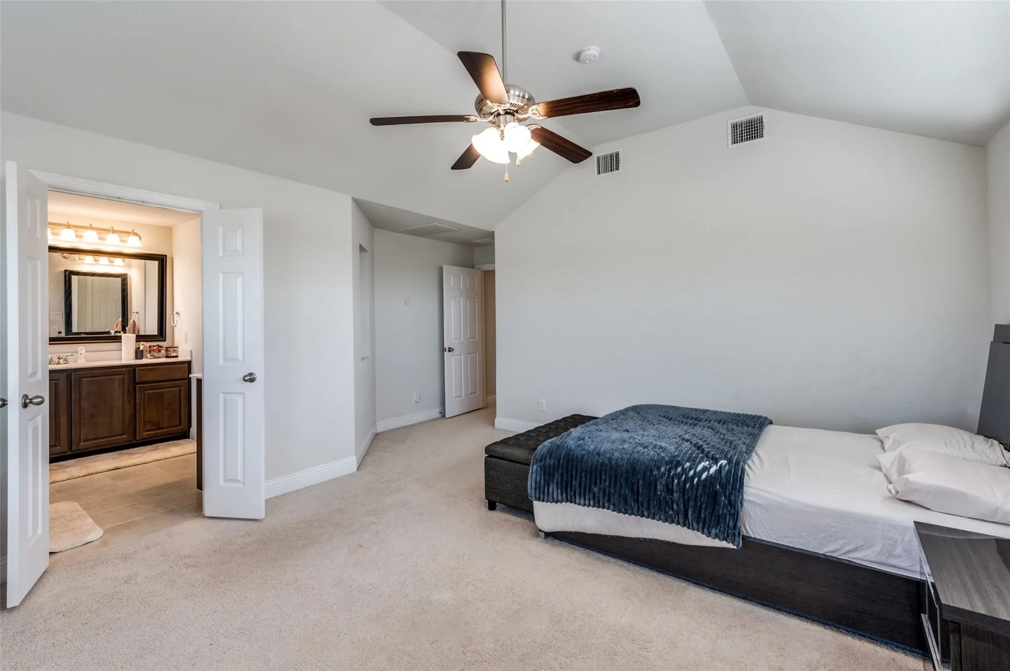 Vaulted ceilings, ceiling fan with integrated lighting, neutral carpet, and a bathroom with a double vanity and framed mirror
