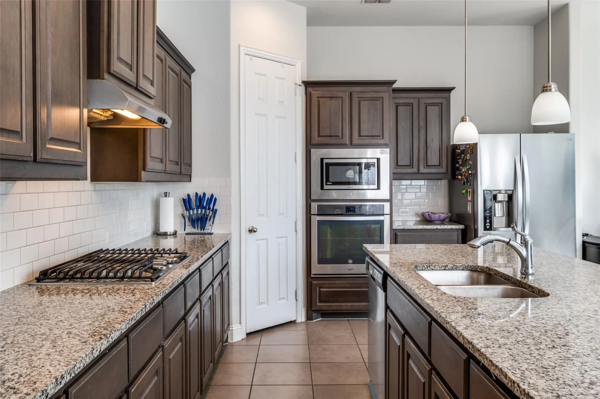 Kitchen featuring dark wood cabinetry, granite countertops, white subway tile backsplash, stainless steel appliances, and tile flooring