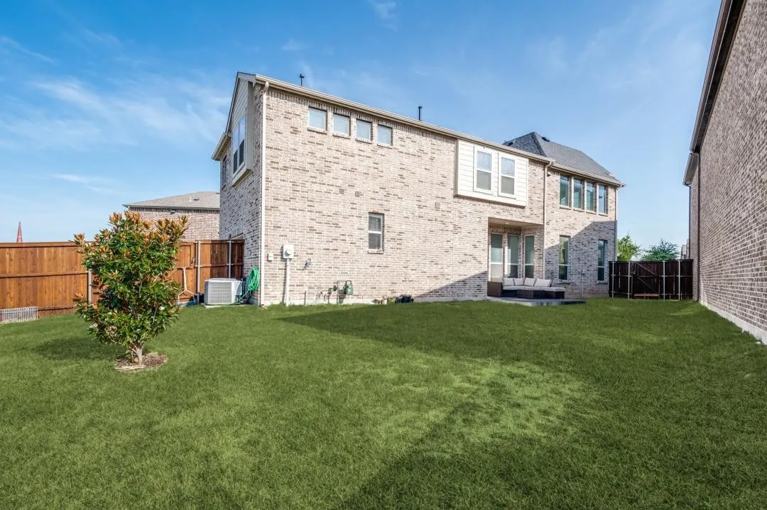 Expansive grass lawn with a brick exterior, privacy fencing, and an outdoor patio