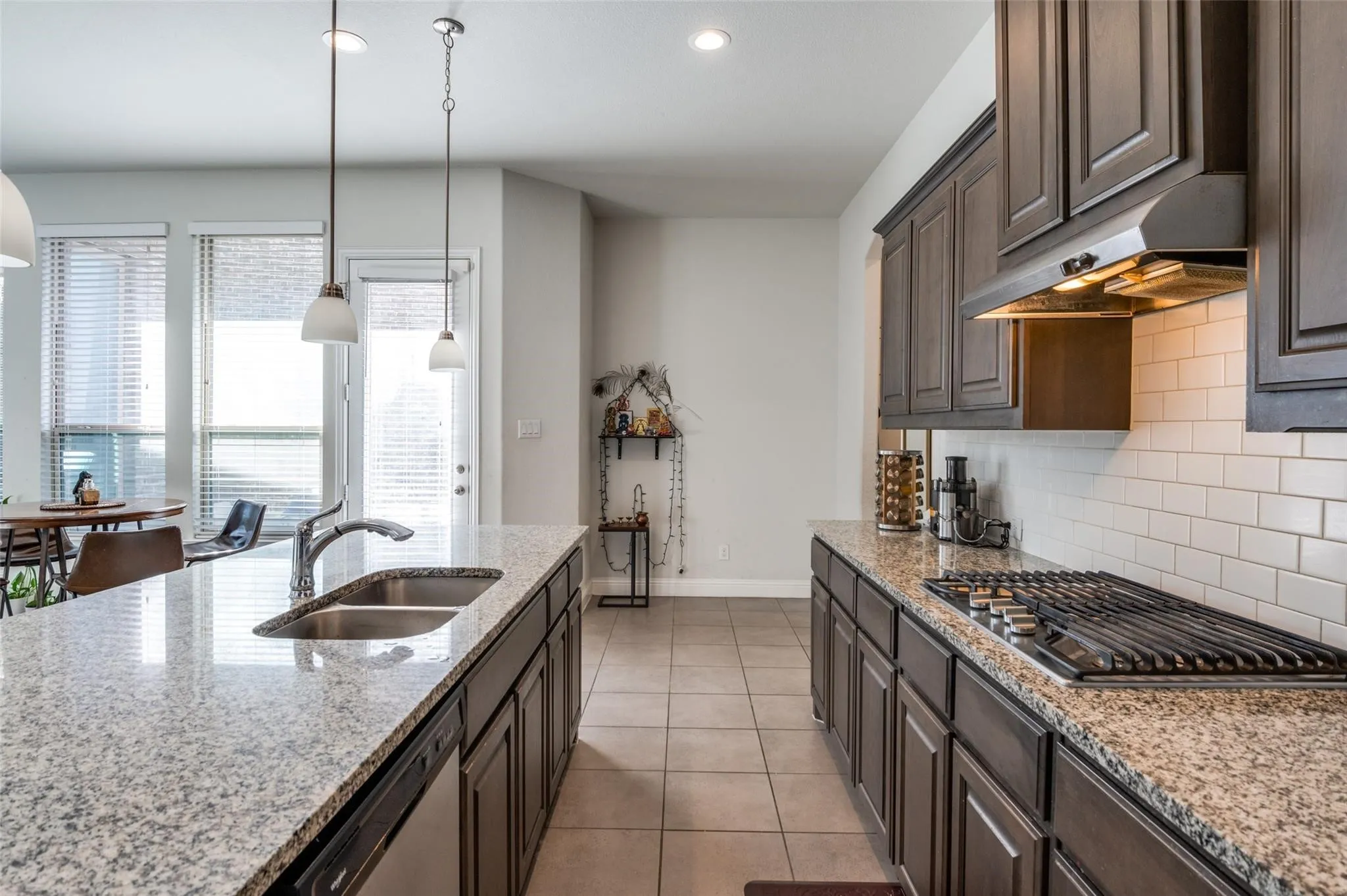 Kitchen featuring granite countertops, dark wood-finish cabinetry, a stainless steel gas range, a dual-basin sink, and white subway tile backsplash
