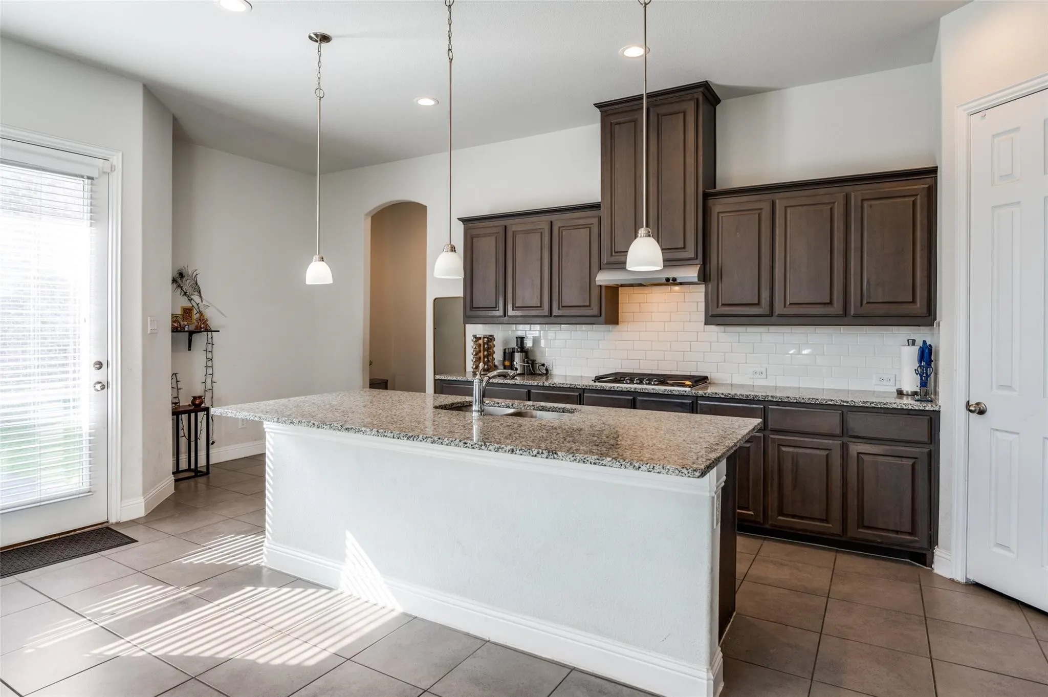 Kitchen featuring an island with a speckled countertop, dark wood-finish cabinetry, a white subway tile backsplash, and stainless steel appliances