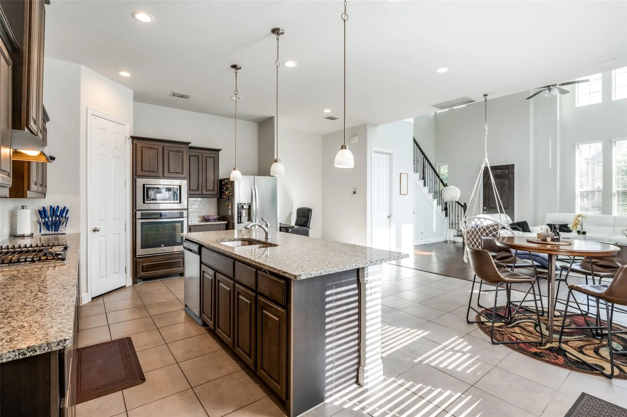 Kitchen featuring an island with a sink, stainless steel appliances, dark wood cabinetry, and granite countertops