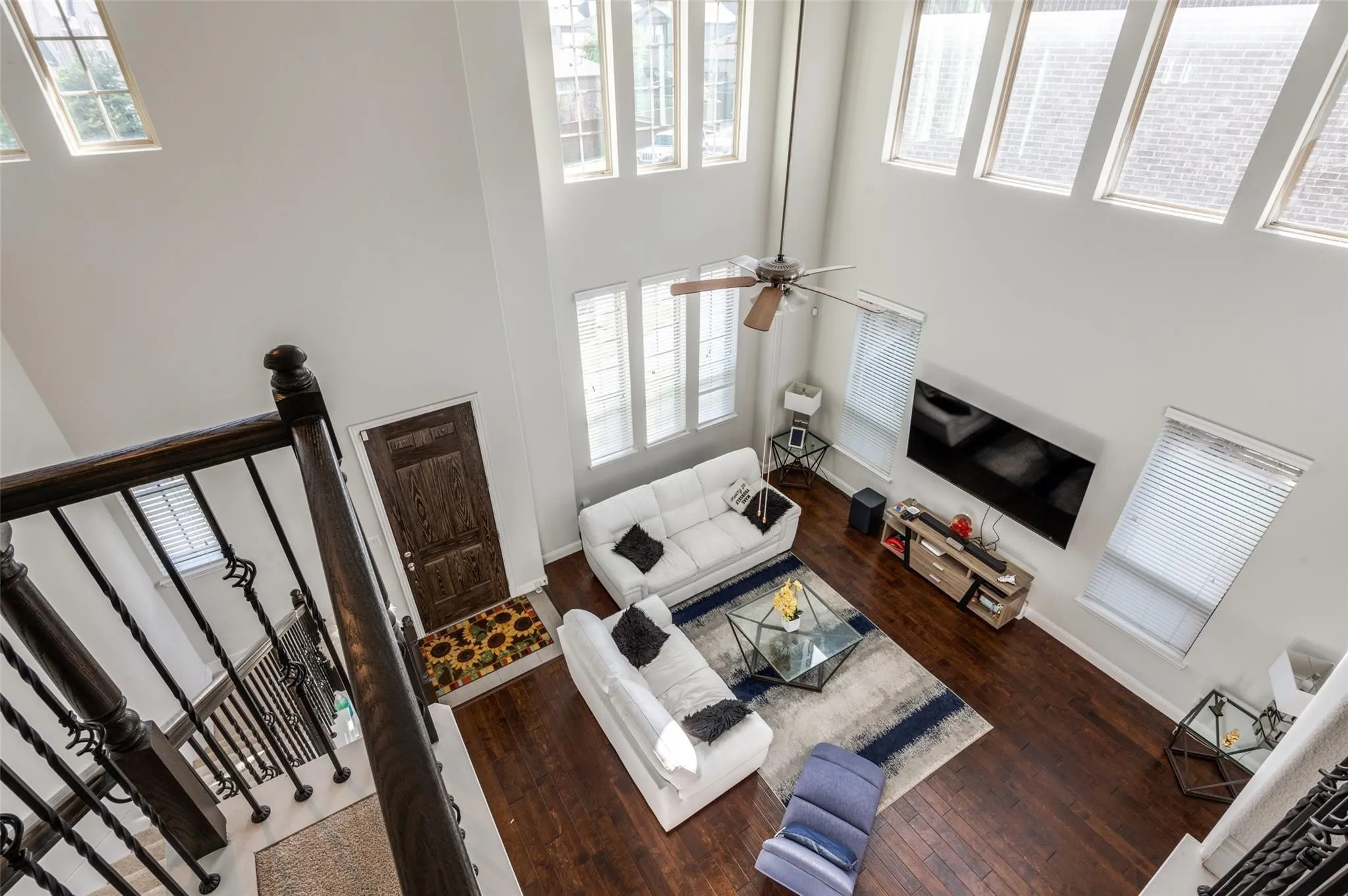 Double-height living space featuring wood-finish flooring, a ceiling fan, and multiple windows