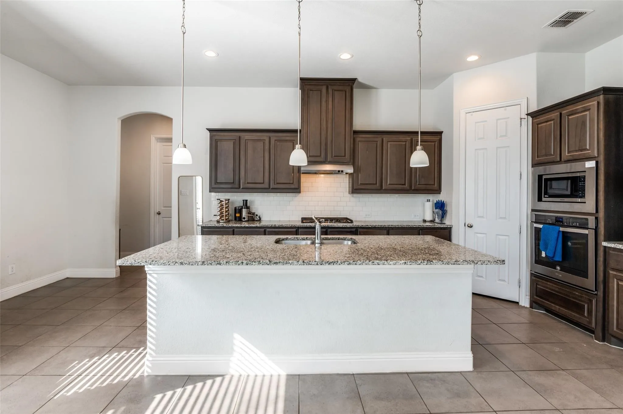 Kitchen with a large island featuring an undermount sink, dark wood cabinetry, stainless steel appliances, and tile flooring throughout