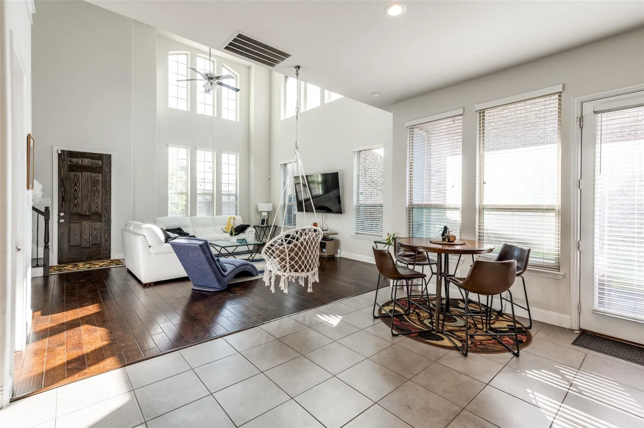 Two-story living area with dark wood-finish flooring, a ceiling fan, and multiple large windows