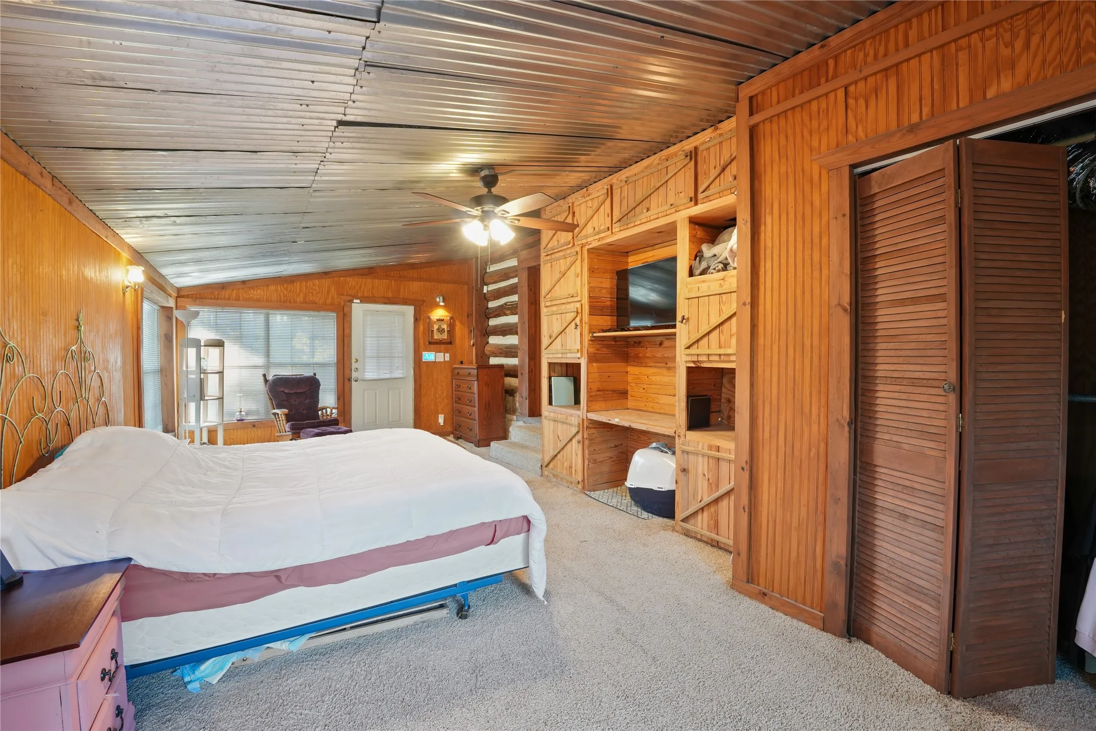 Corrugated metal ceiling, wood-paneled walls, built-in shelving, louvered bi-fold closet doors, and a ceiling fan