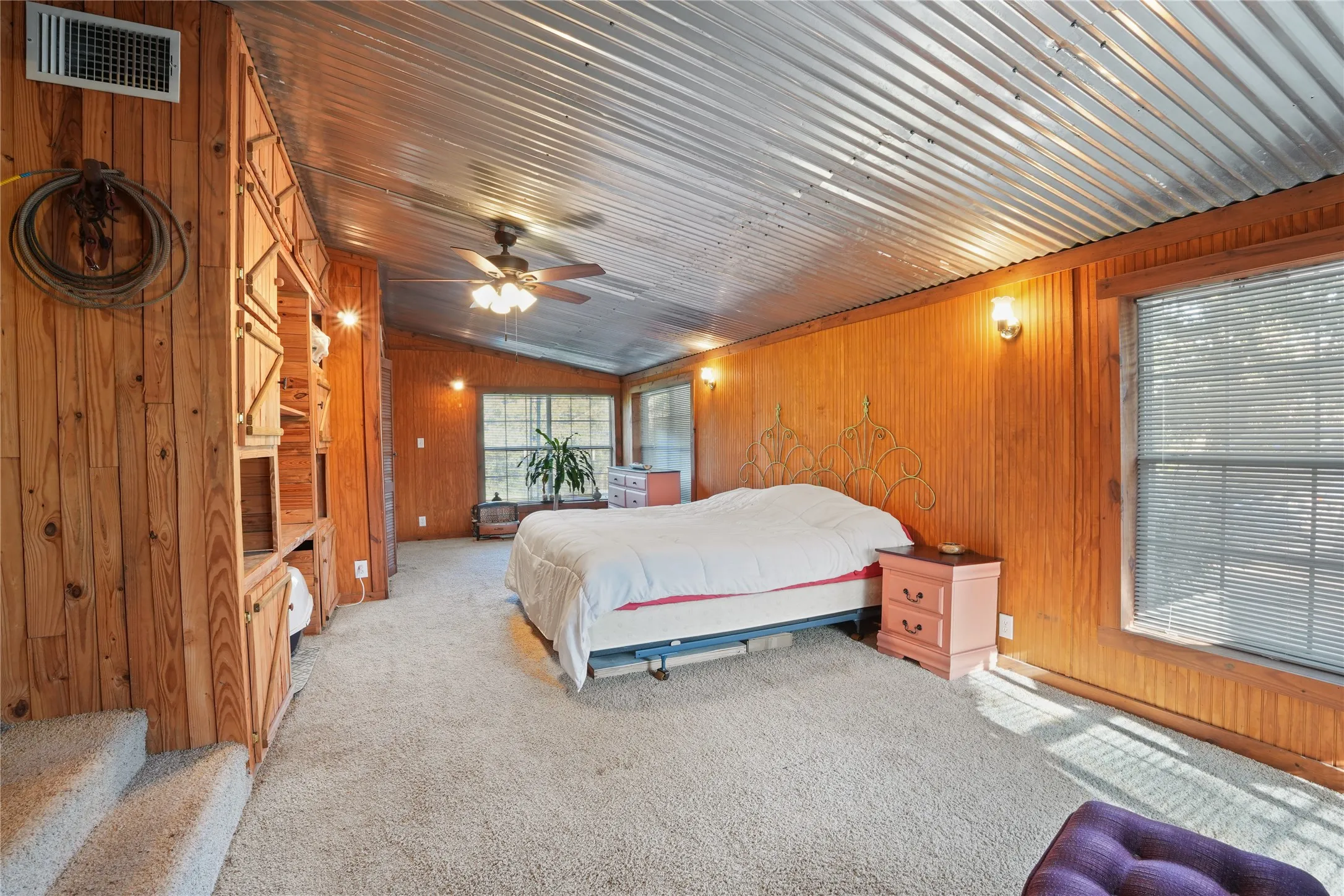 Corrugated metal ceiling, wood paneling, carpet flooring, built-in shelving, and a ceiling fan with integrated lighting