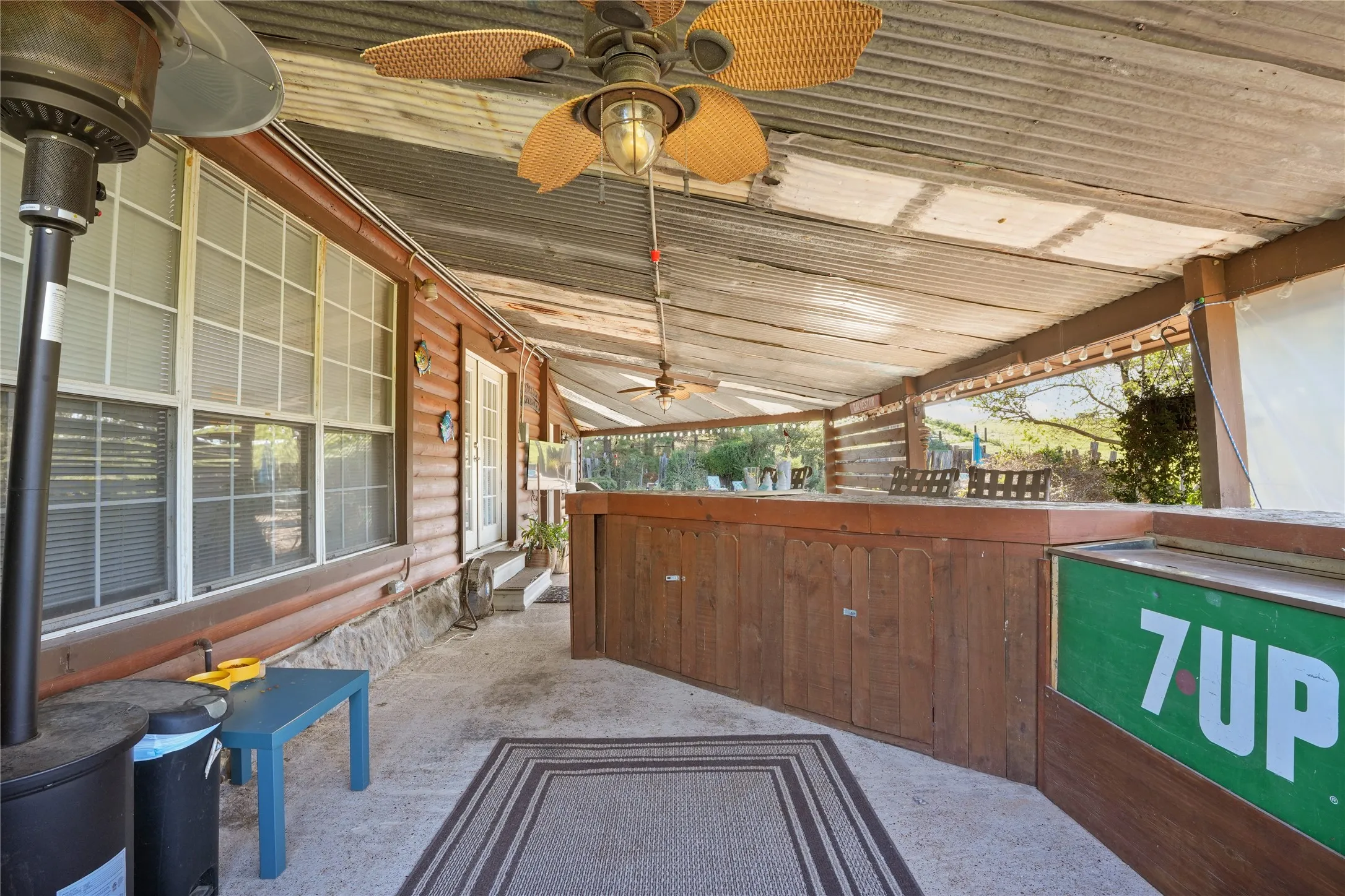 Covered outdoor patio featuring a corrugated metal roof, wood-paneled walls, and multiple ceiling fans