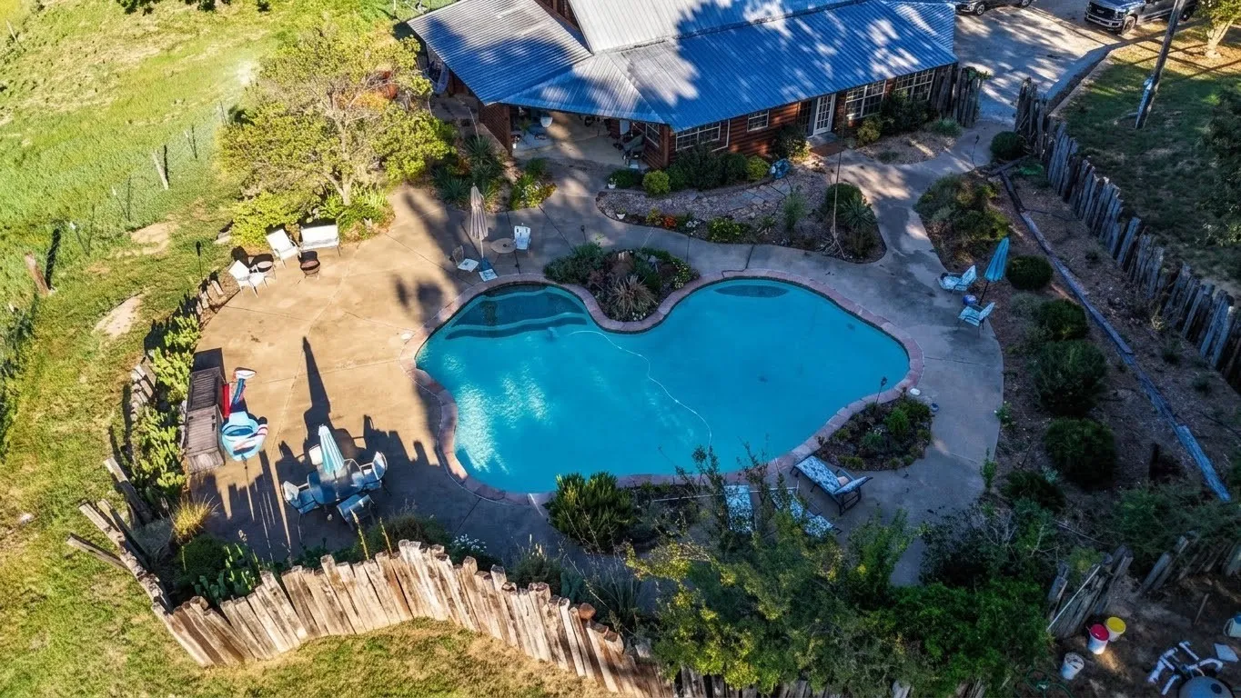 Freeform swimming pool with surrounding concrete patio and landscaping