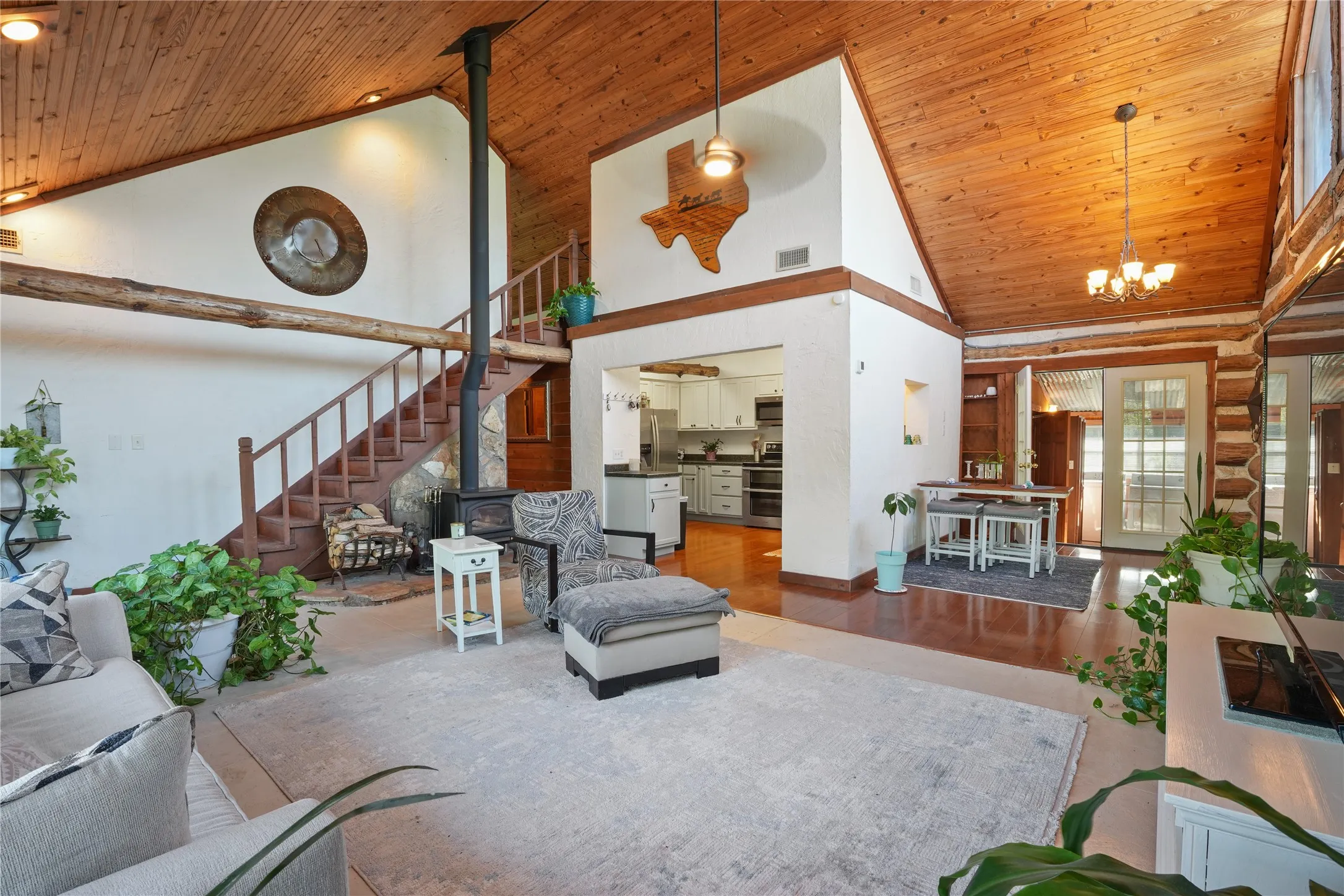 Vaulted wood-paneled ceiling, wood stove with stone surround, open-tread wood staircase, wood-finish flooring, and white French doors