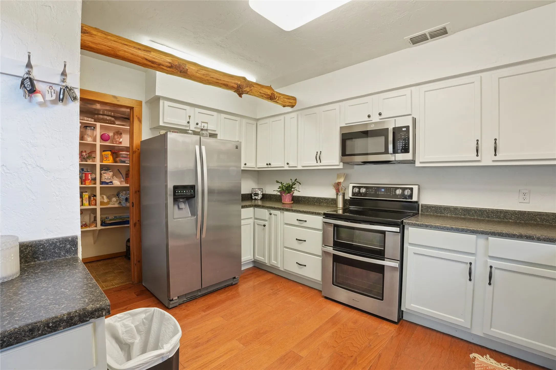 Vaulted wood-paneled ceiling, exposed log walls, stone hearth with a wood stove, upper-level windows, and a built-in kitchen