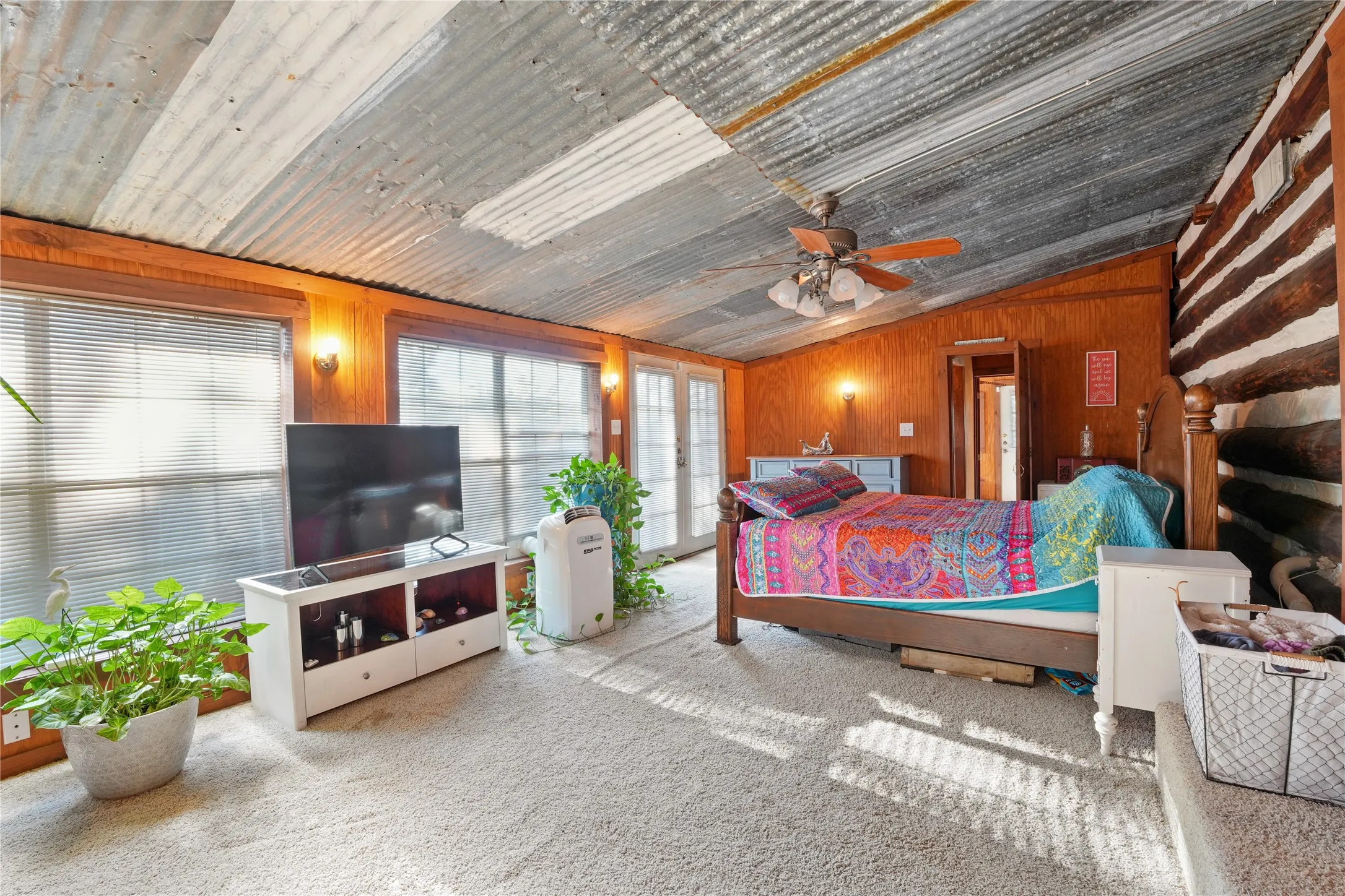 Corrugated metal ceiling, wood-paneled walls, French doors, multiple windows with blinds, and a log-style accent wall