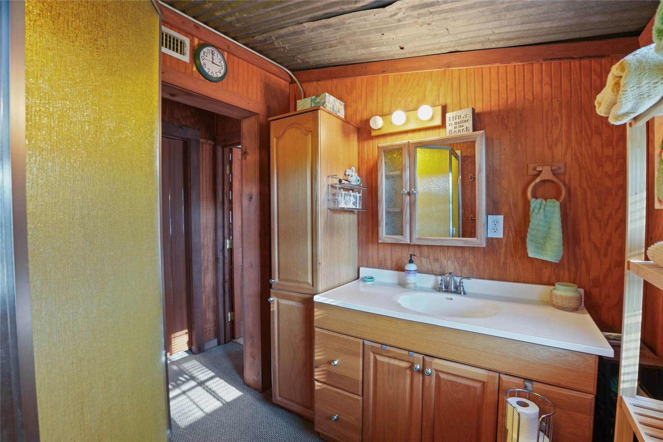 Wood-paneled walls and ceiling, built-in wooden vanity with integrated sink, chrome-finish faucet, wall-mounted medicine cabinet with mirror, and built-in linen storage