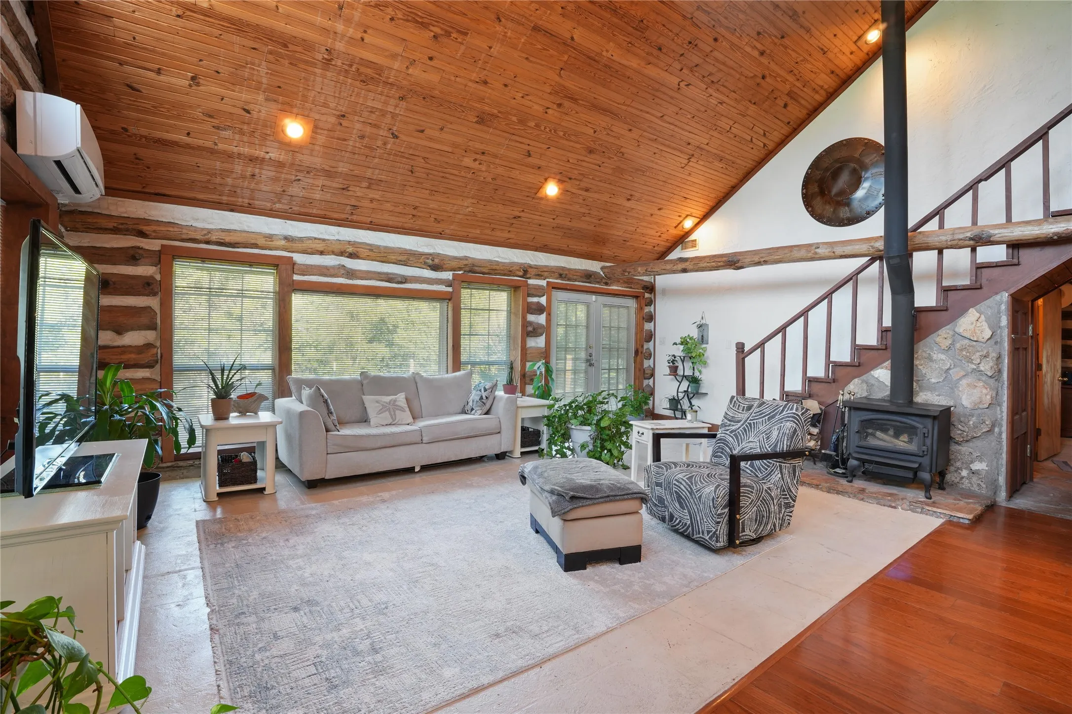 Vaulted wood-paneled ceiling, exposed log walls, stone-clad fireplace, wood-finish flooring, and a built-in staircase