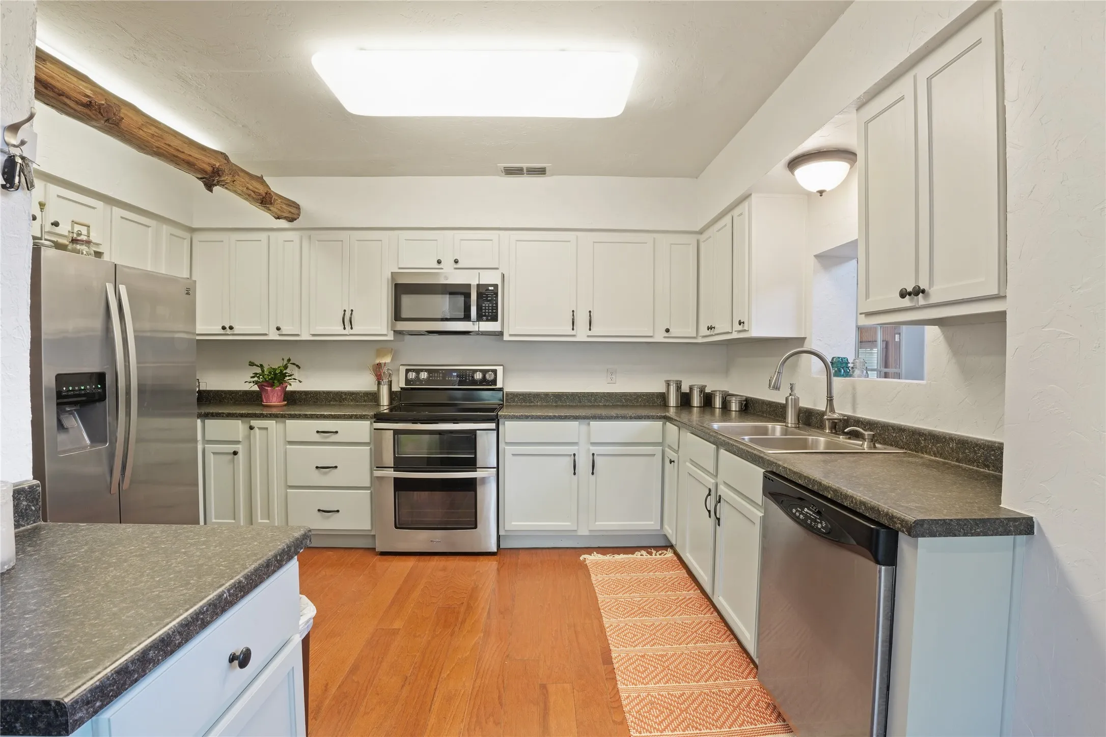 Kitchen featuring wood-finish flooring, white cabinetry with dark hardware, stainless steel appliances, and dark countertops