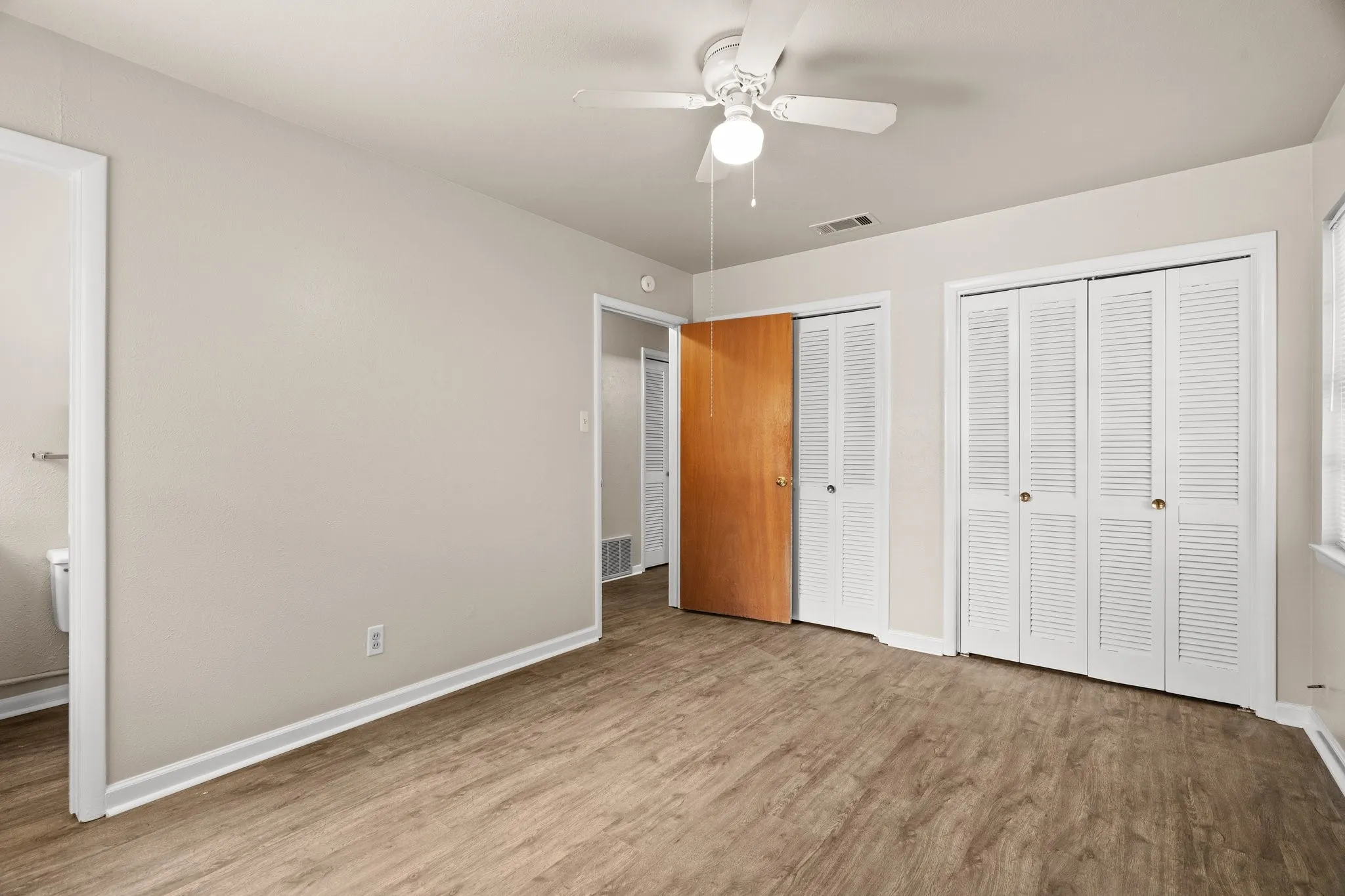 Unfurnished bedroom with ceiling fan, light wood-type flooring, and two closets