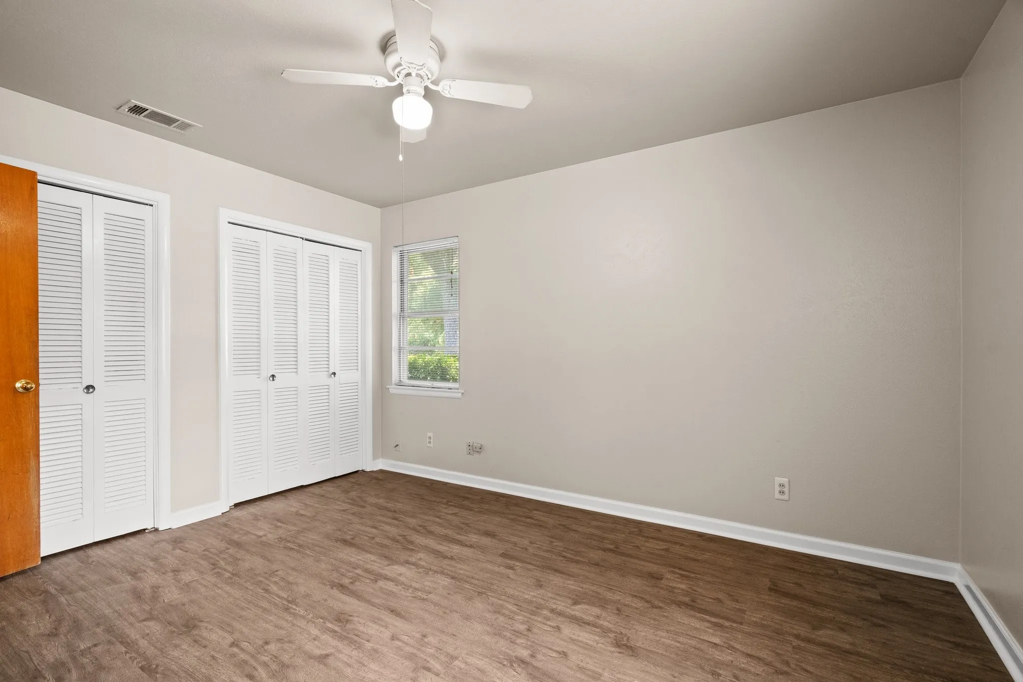 Unfurnished bedroom with wood-type flooring, ceiling fan, and multiple closets