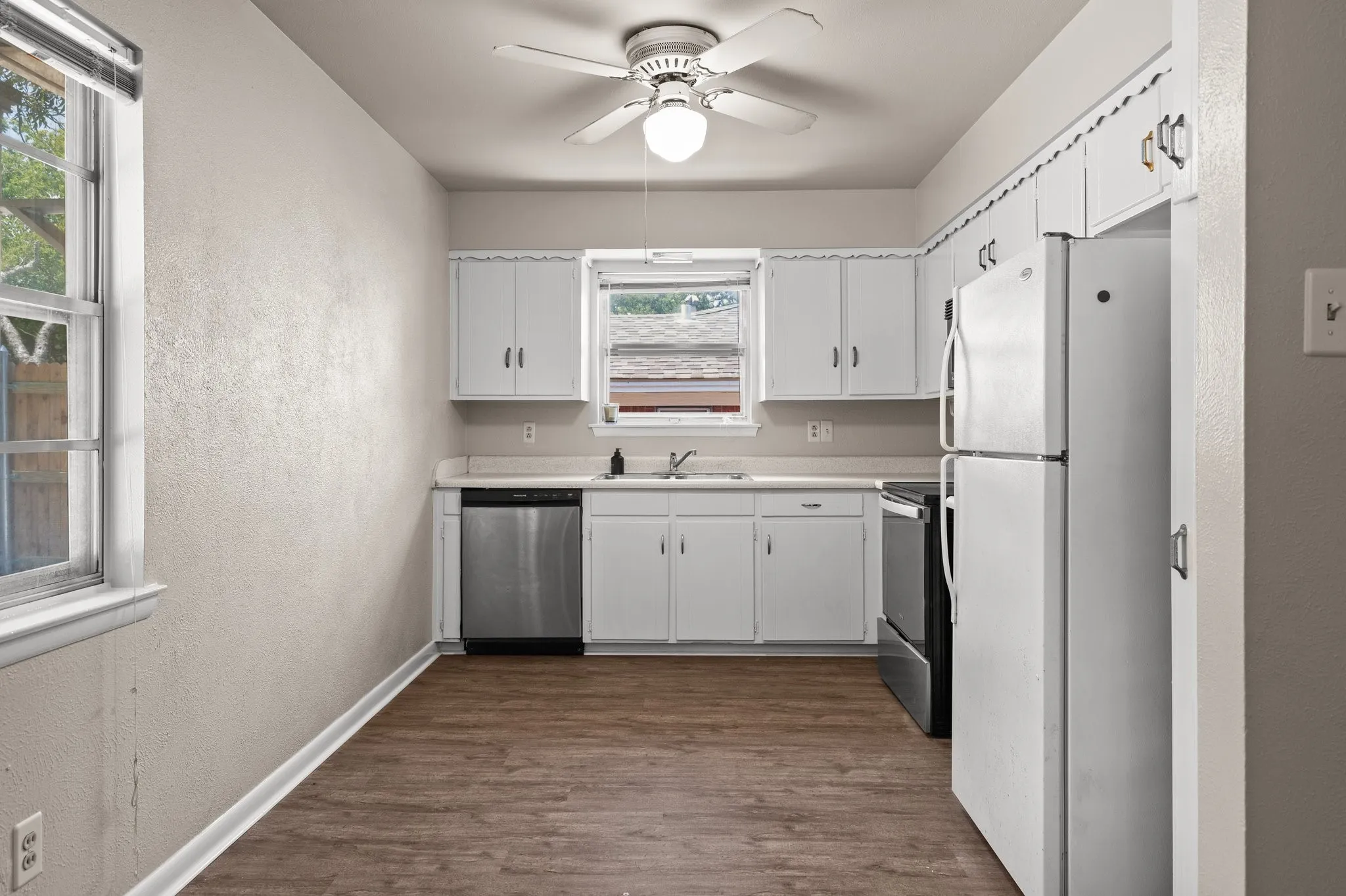 Kitchen featuring dark wood-type flooring, sink, white cabinets, appliances with stainless steel finishes, and ceiling fan