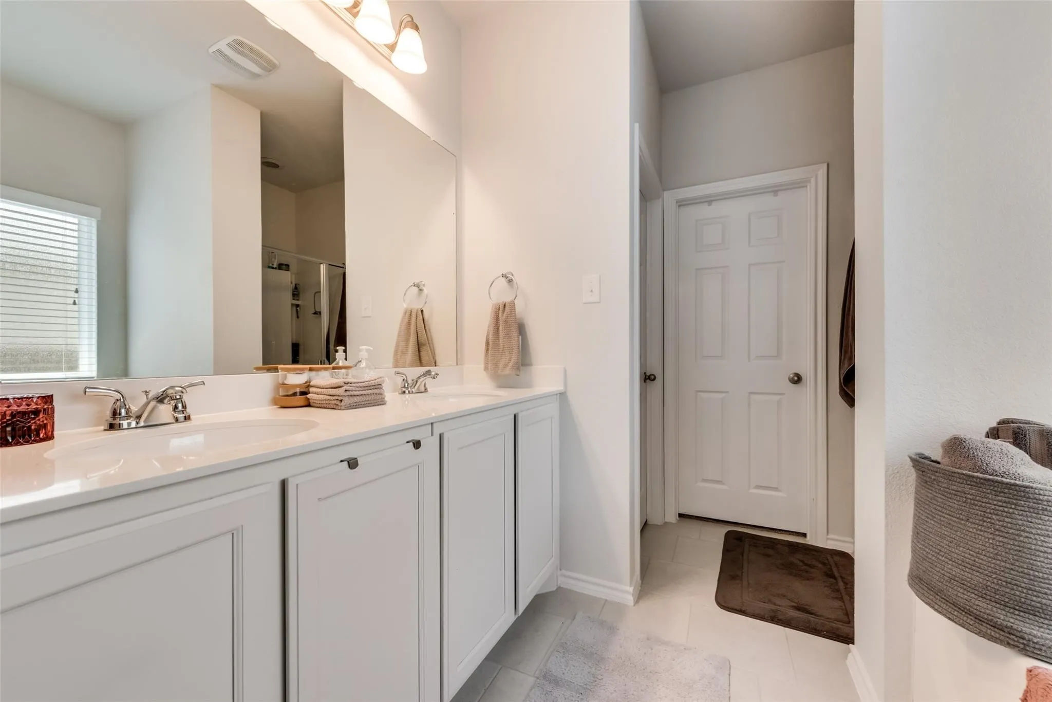Double vanity with white cabinetry, polished chrome fixtures, and a large mirror