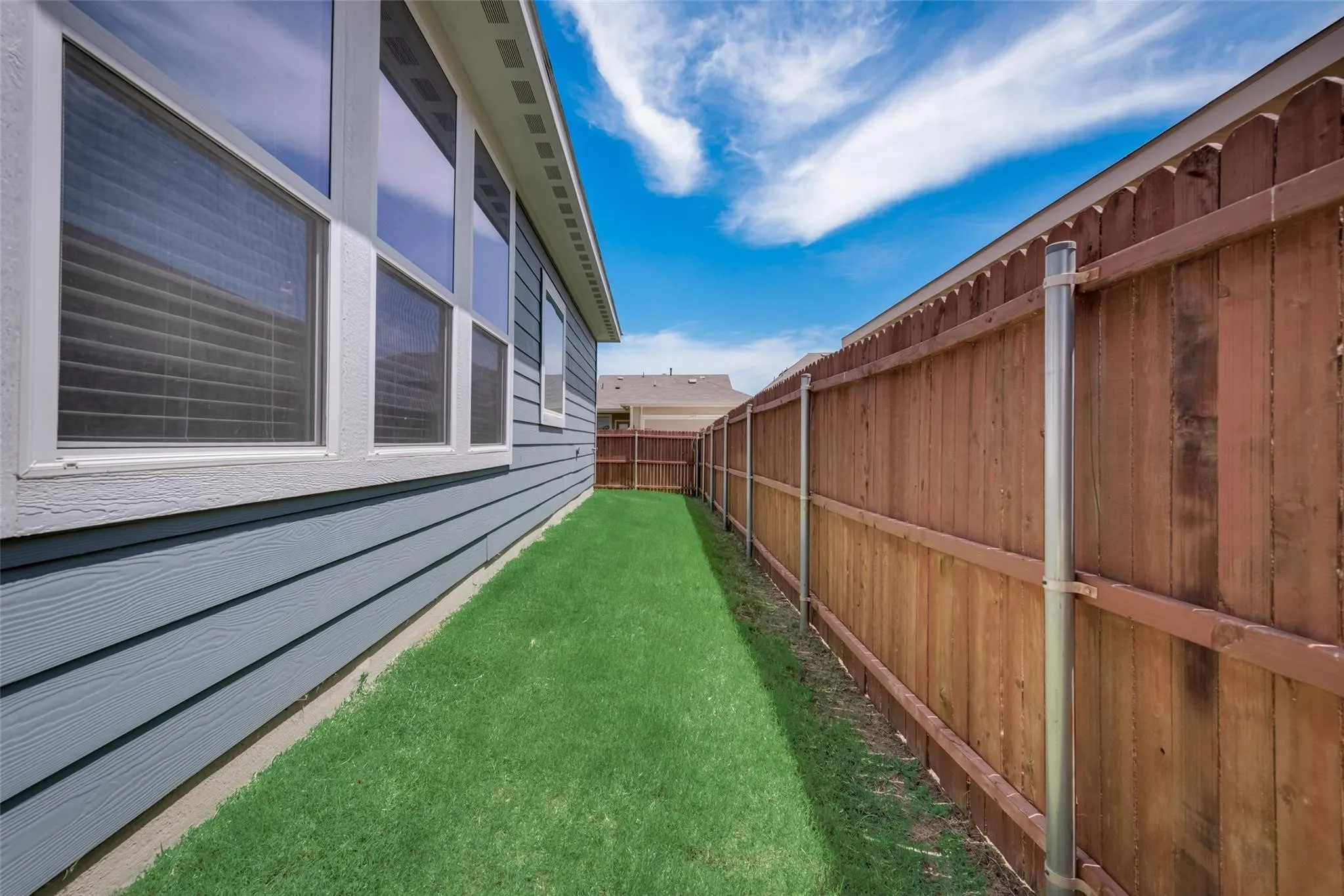 Side yard featuring a manicured lawn, wood-panel fencing, and a house exterior with blue siding