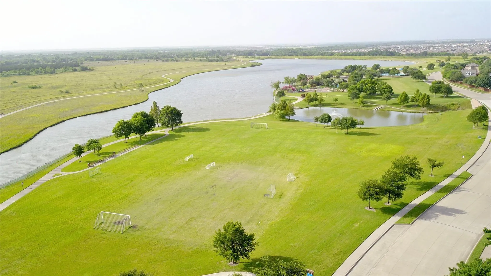 Expansive grassy areas, large body of water, walking paths, paved road, and scattered trees