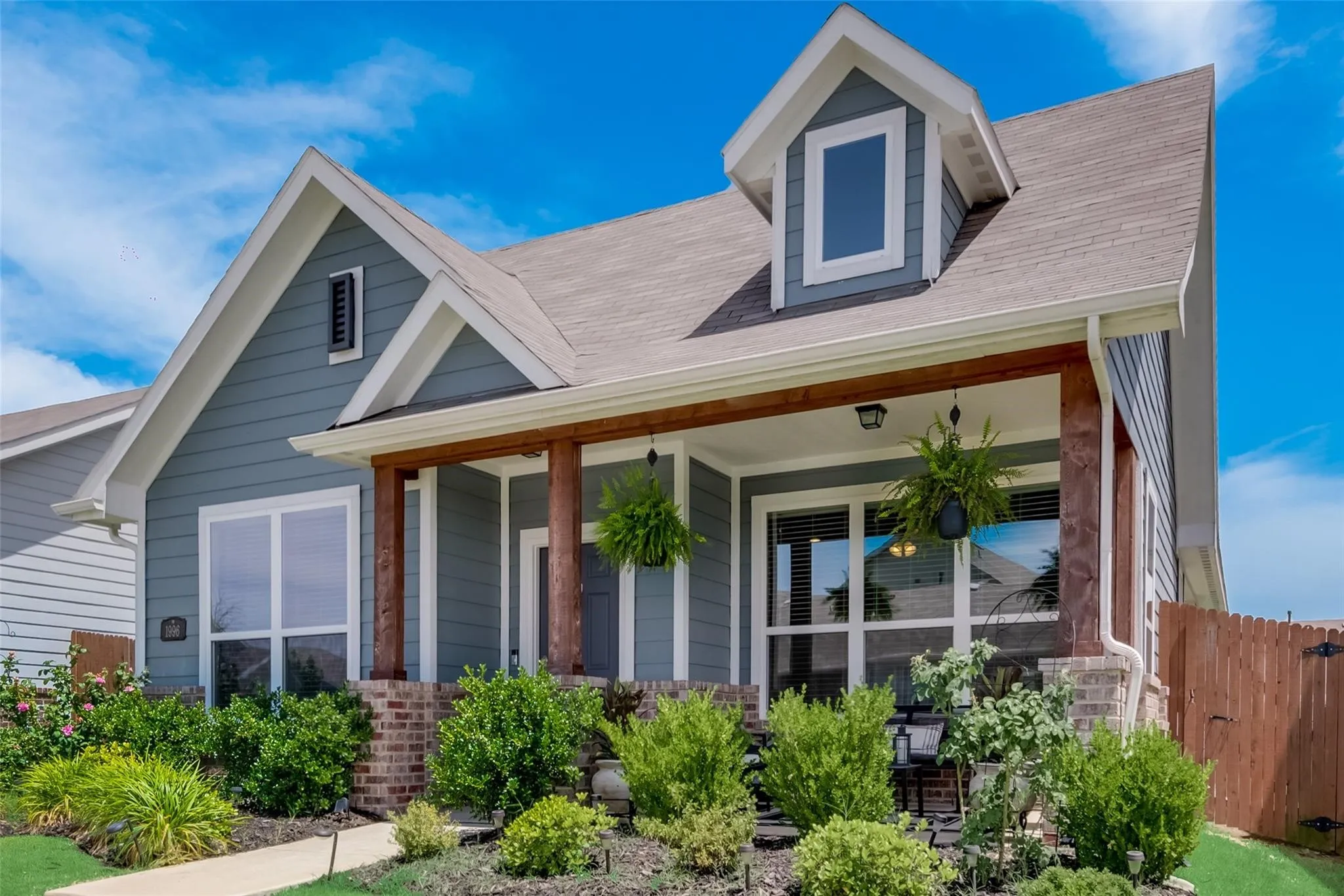 Exterior featuring blue siding, white trim, a dormer window, wood-look porch columns, and a brick base