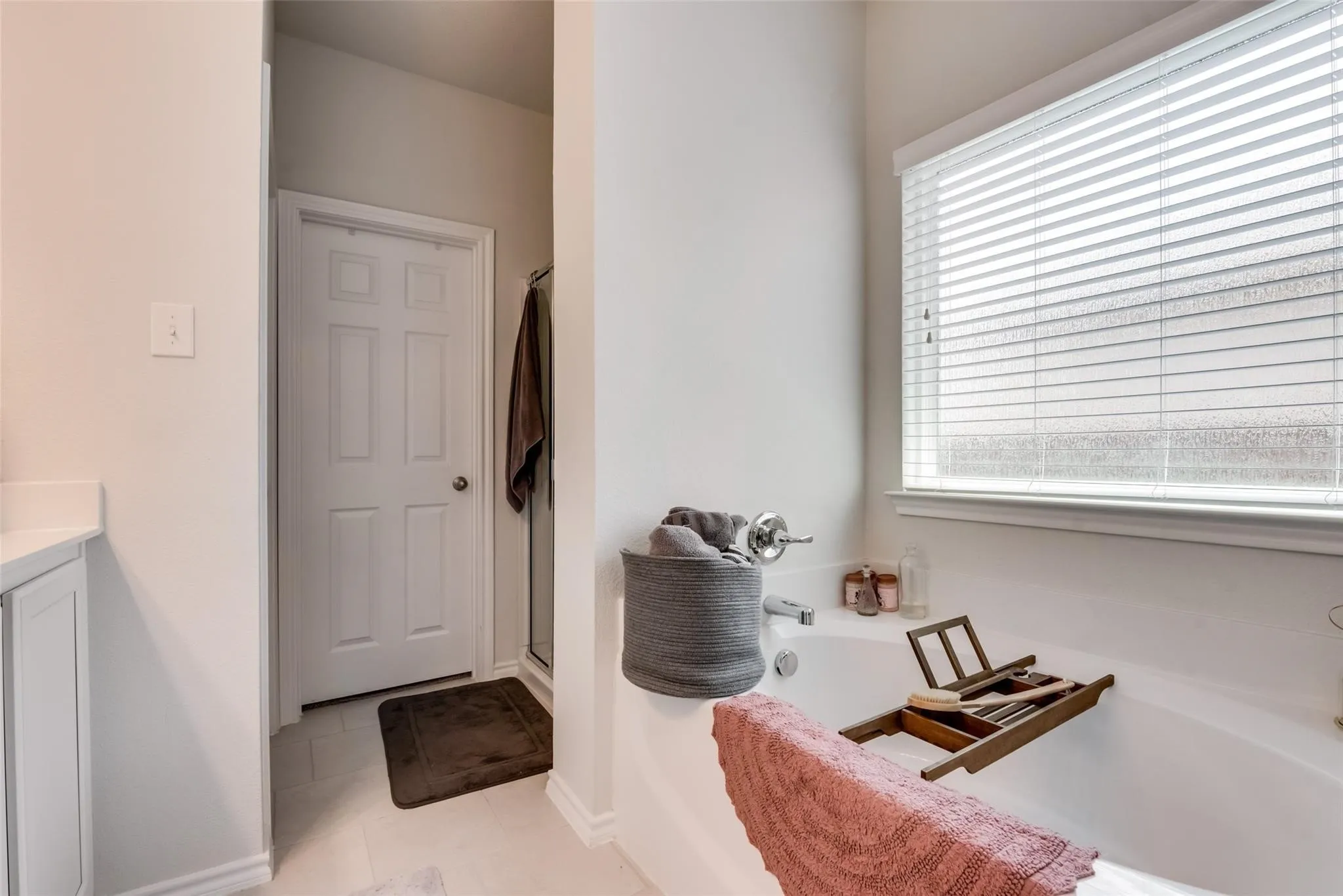 Built-in soaking tub with chrome fixtures, white window blinds, and light-toned wall paint