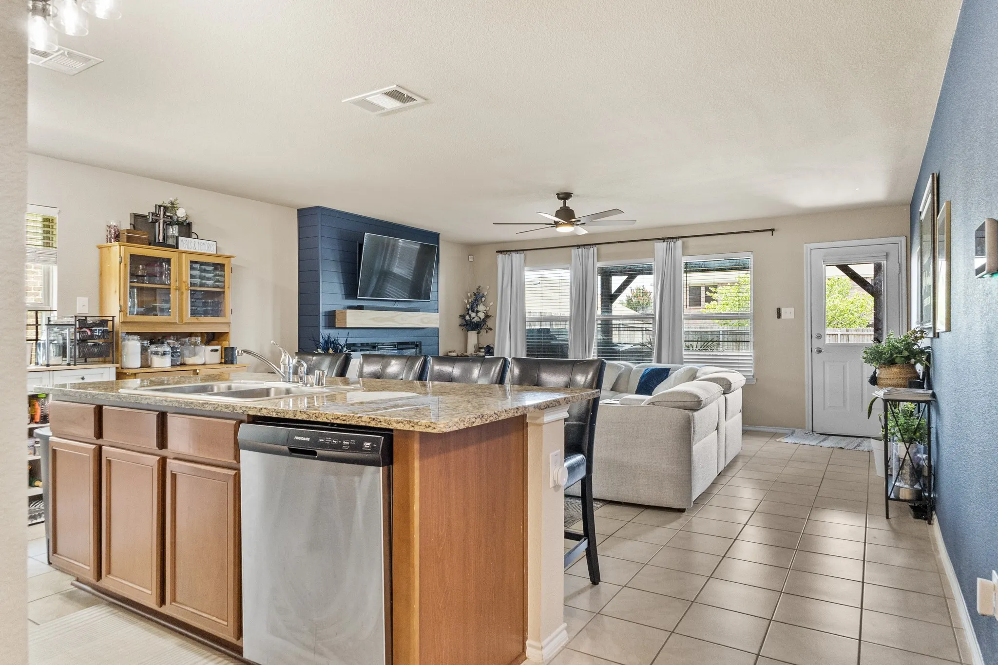 Kitchen island with granite countertop and integrated sink, stainless steel dishwasher, and wood-finish cabinetry