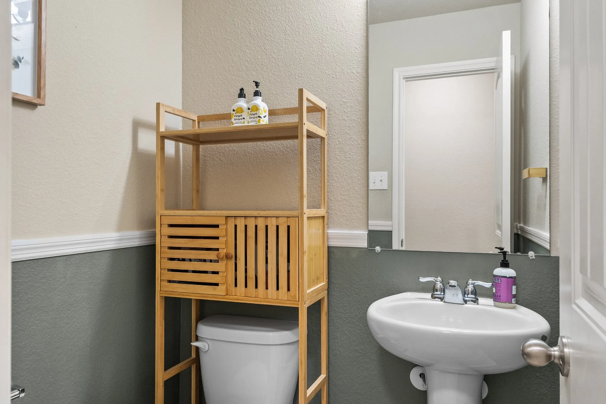 Pedestal sink with chrome fixtures, full-width wall mirror, and two-tone wall treatment with chair rail molding
