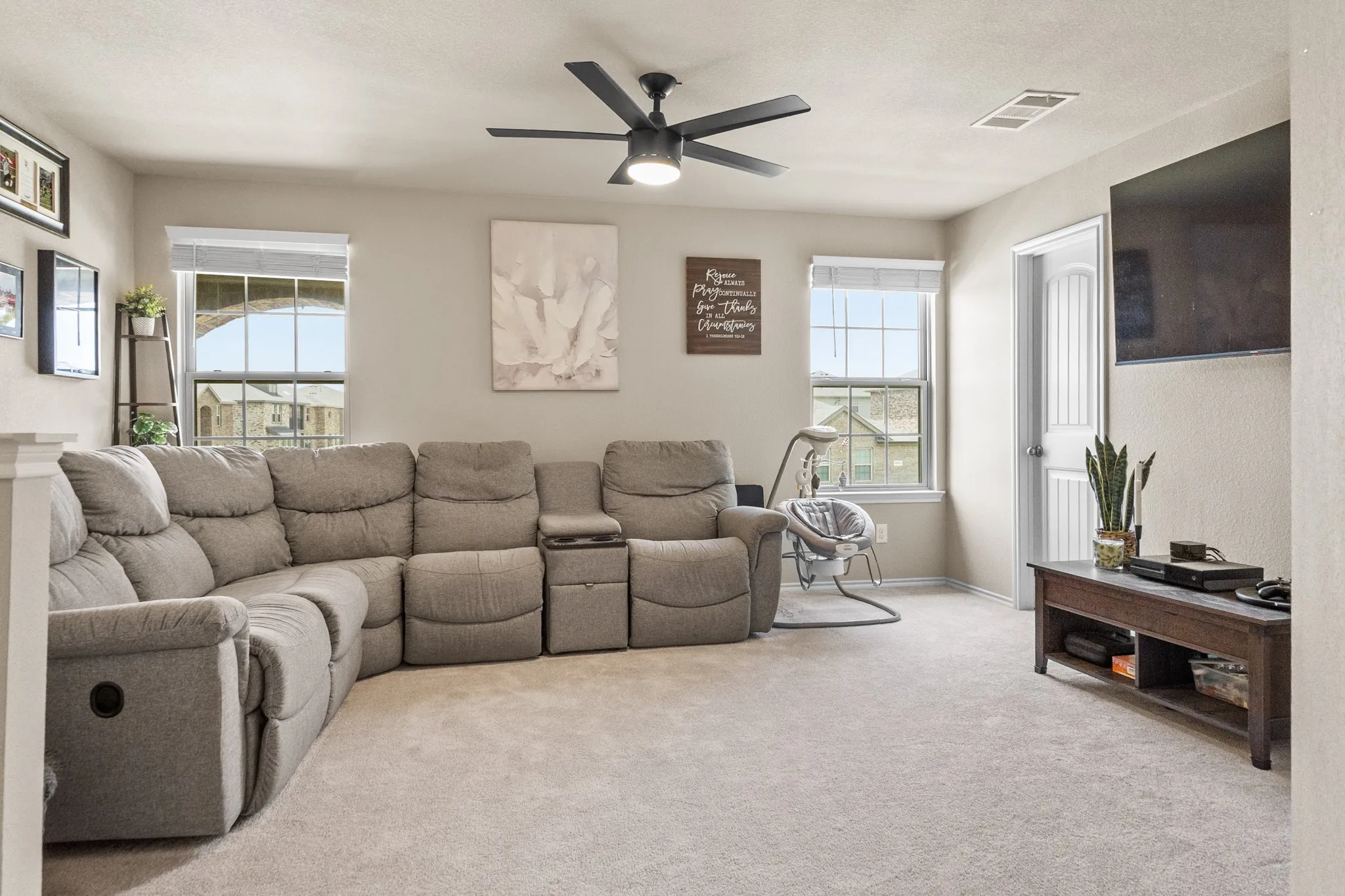 Carpeted living area featuring multiple windows providing natural light, a ceiling fan with integrated lighting, and a white paneled interior door