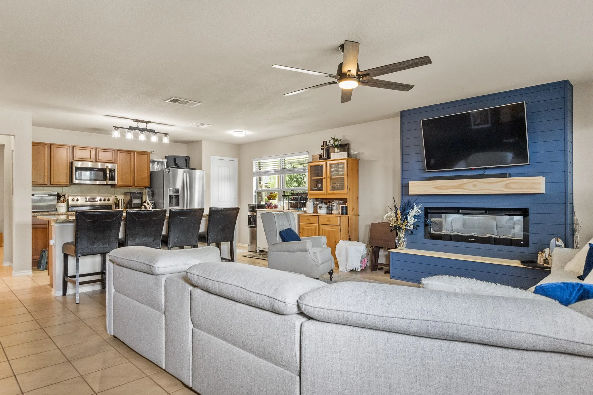 Open-concept living area featuring a modern electric fireplace with a wood mantle, a blue shiplap accent wall, and a ceiling fan