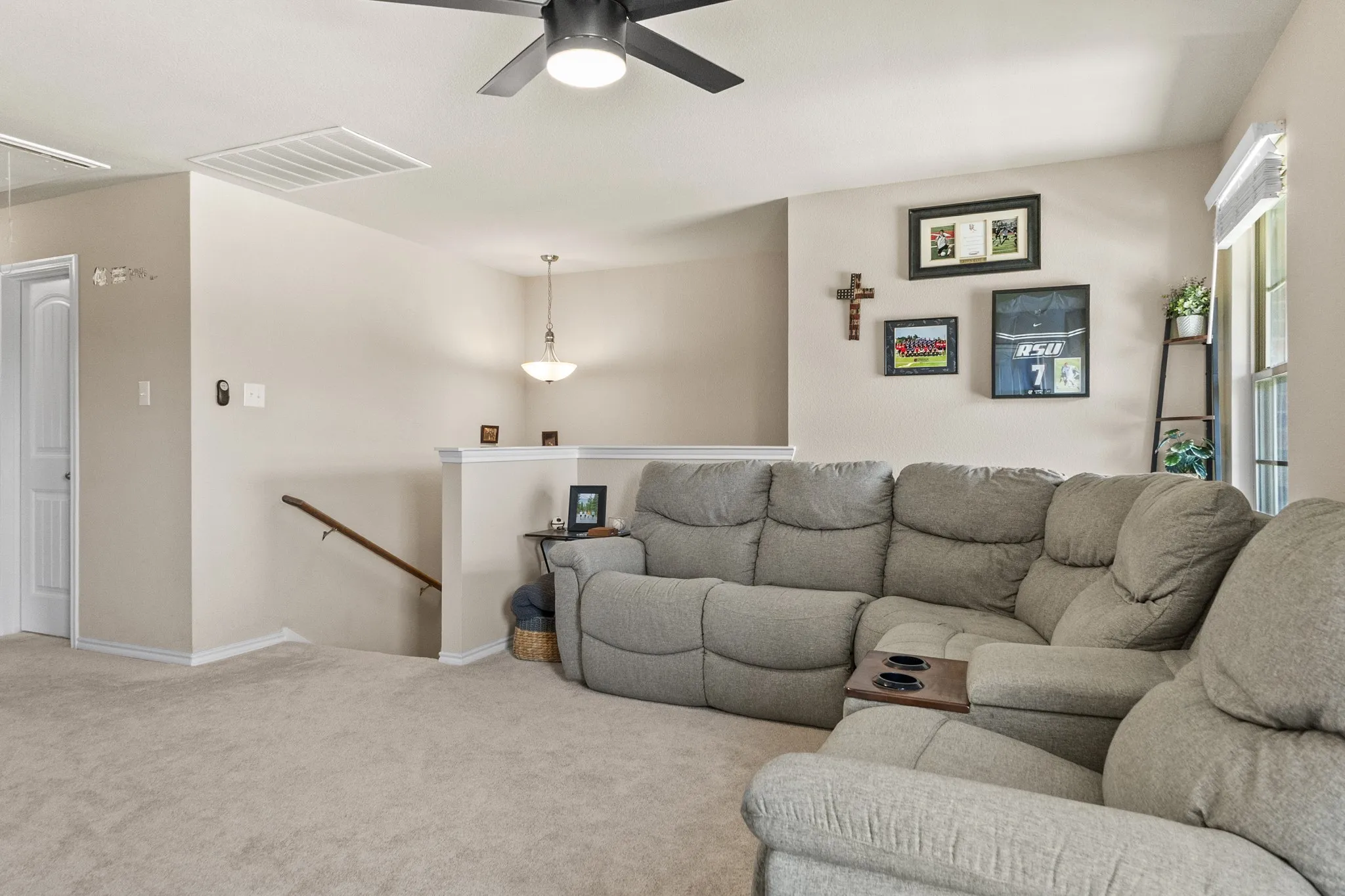 Carpeted upper-level landing featuring a ceiling fan with integrated lighting, a white painted railing, and a window with a roller shade