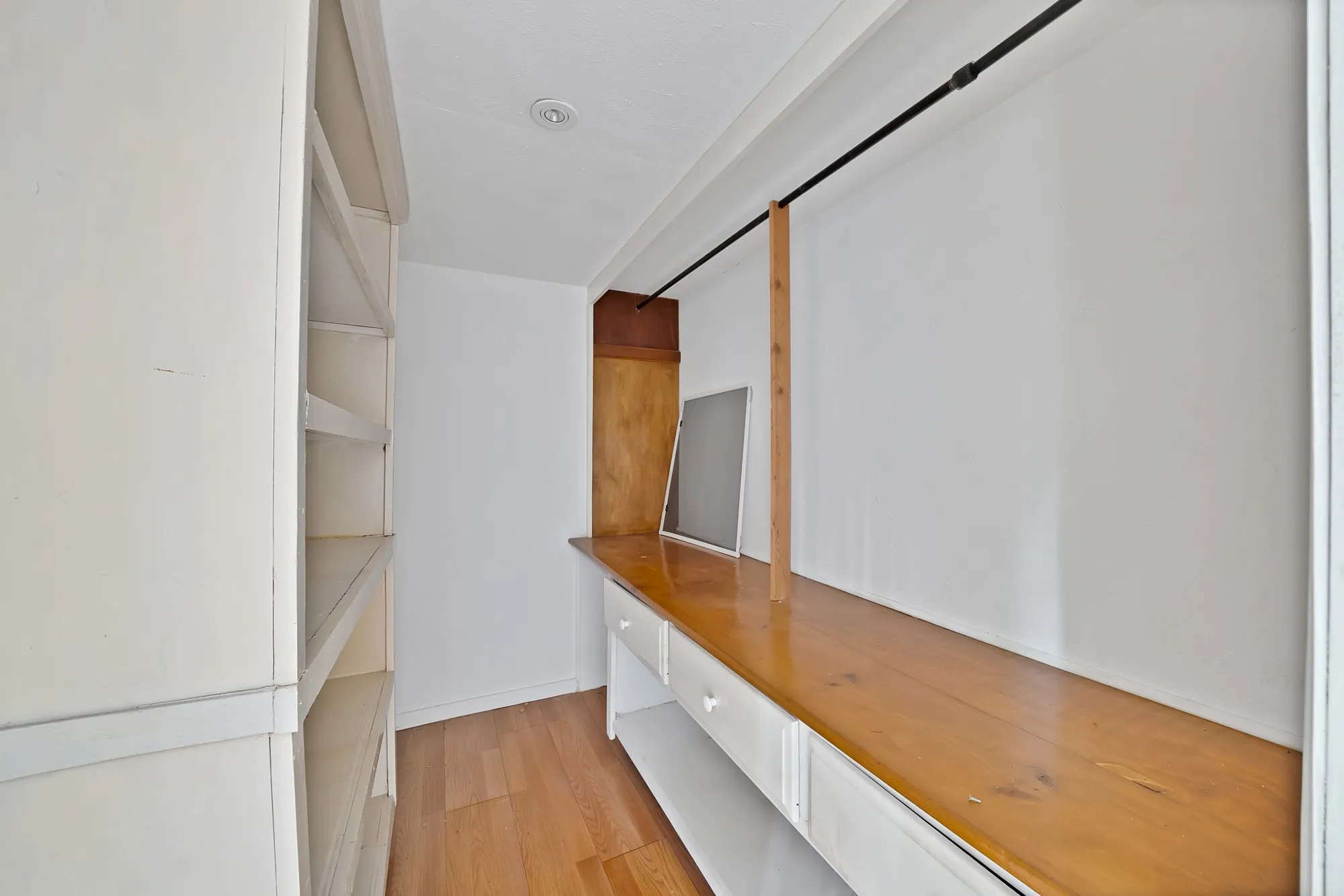 Built-in shelving, wood-finish flooring, built-in desk with drawers, overhead recessed lighting, and a built-in hanging rod