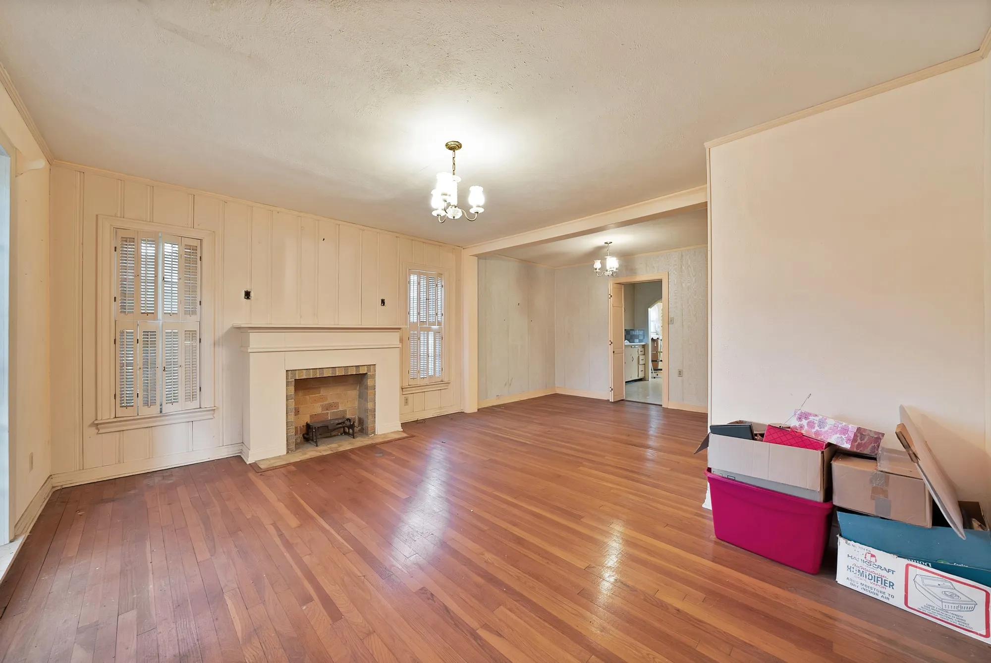 Hardwood flooring, central fireplace with brick interior, dual windows with louvered shutters, and ceiling-mounted light fixtures