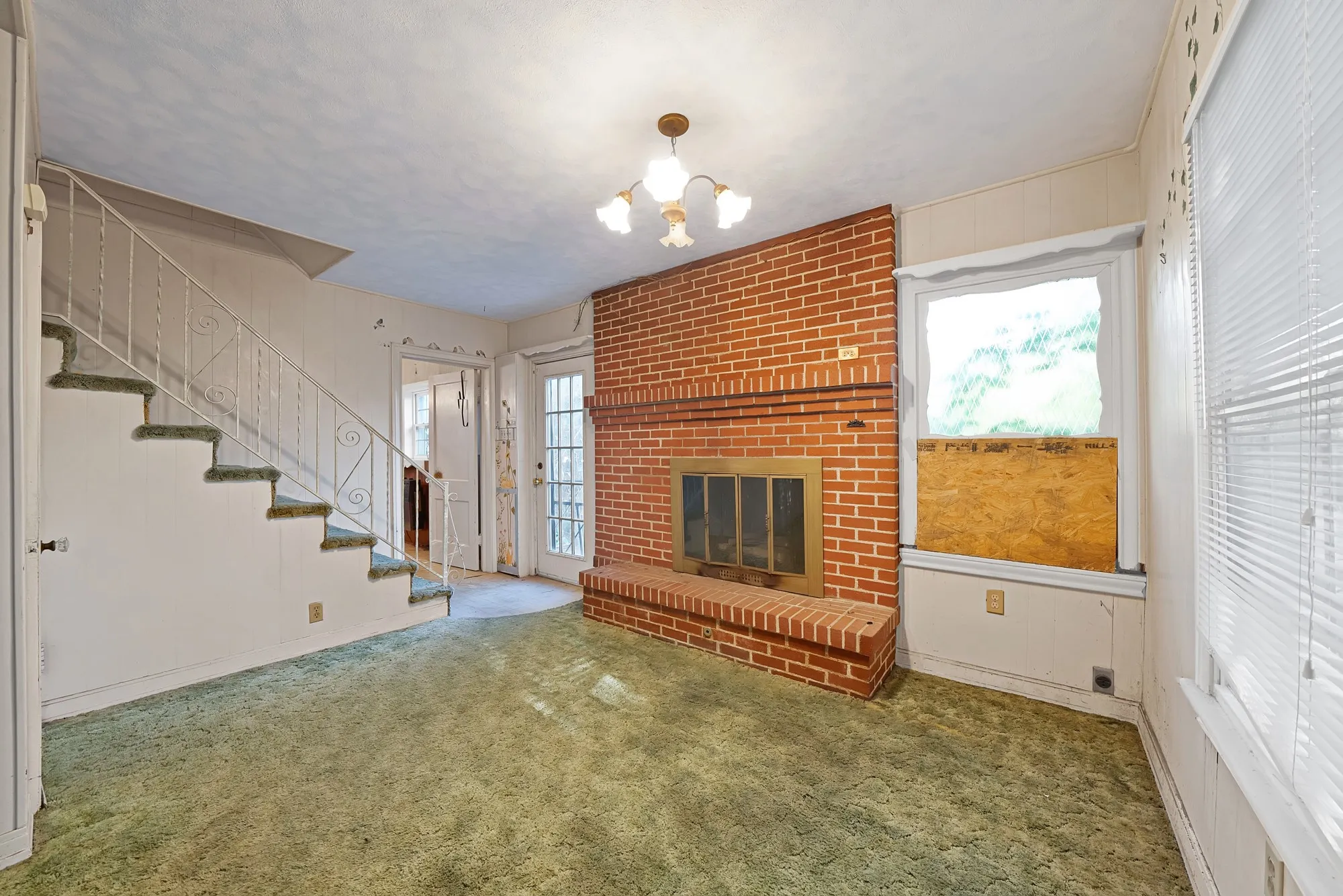 Brick fireplace with a brass firebox, staircase with decorative metal railing, and a glass-paneled exterior door