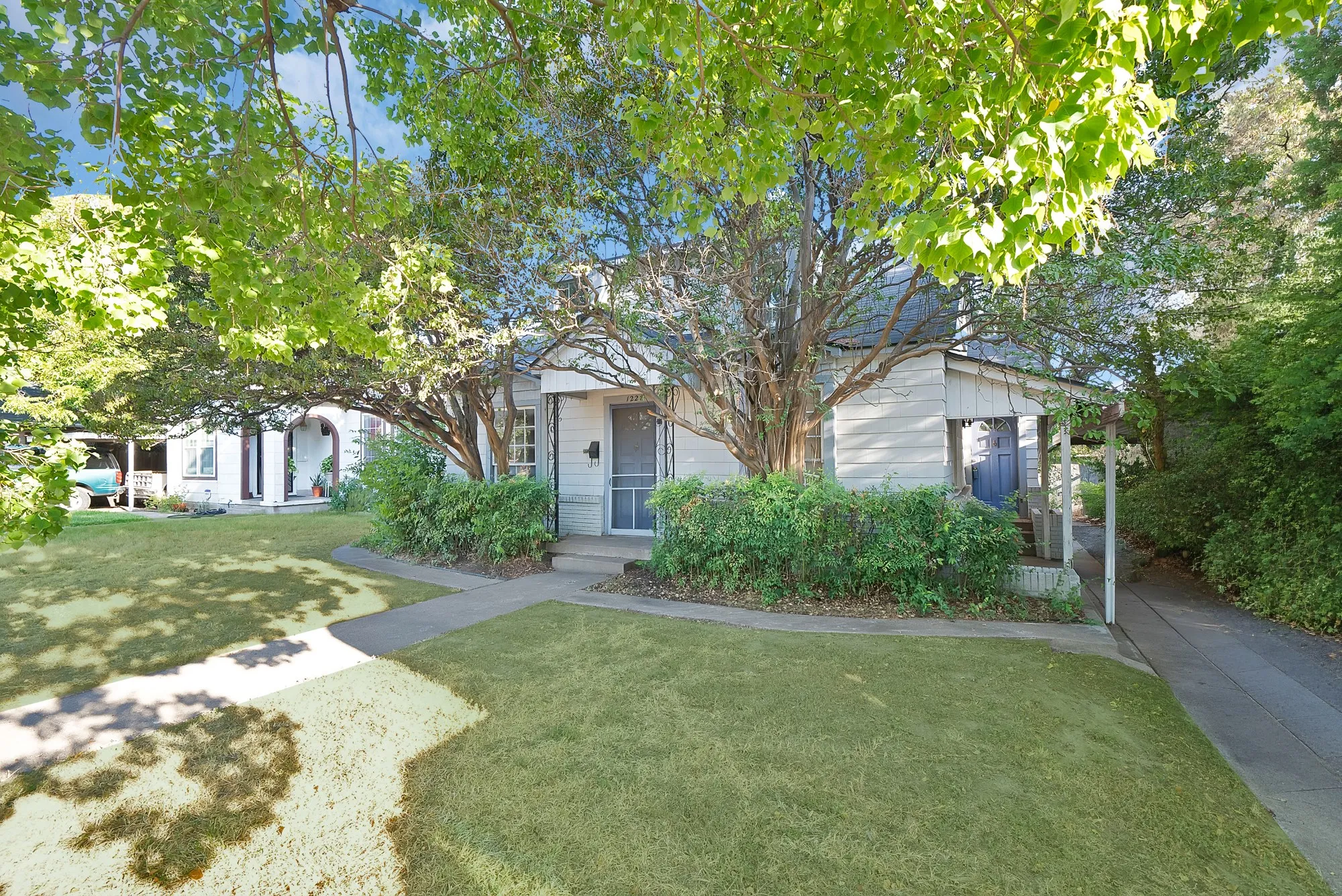 Expansive front lawn with mature shade trees, concrete walkway, and covered front porch with screen door