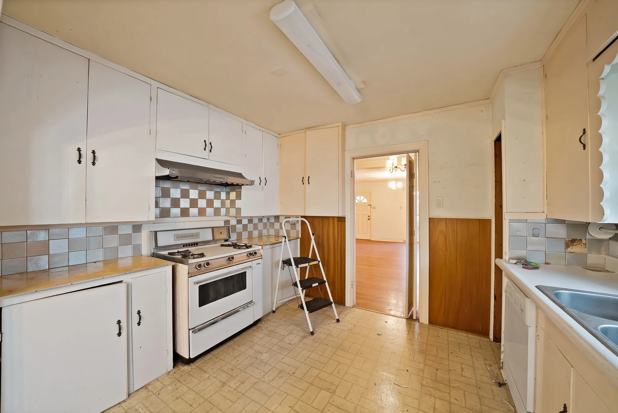 White cabinetry, tile backsplash, built-in range, dual basin sink, wood paneling