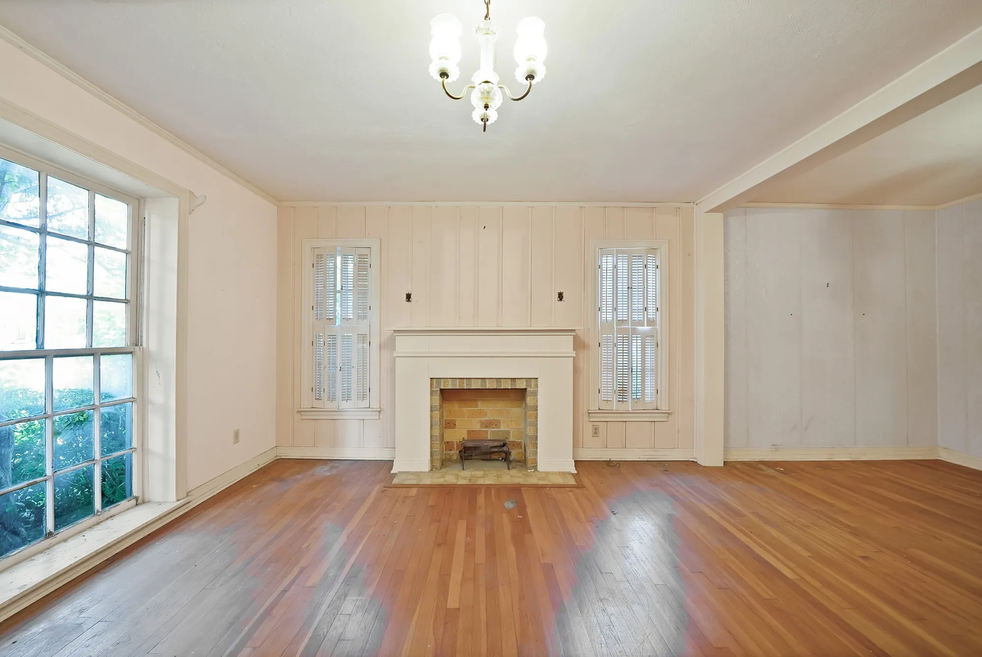 Hardwood flooring, brick fireplace with a white mantel, ceiling-mounted light fixture, and large multi-pane windows