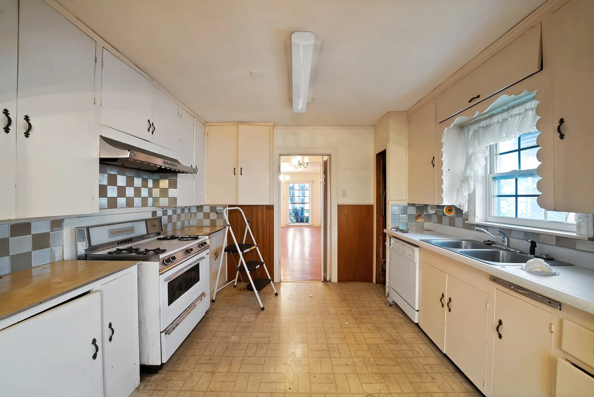 Kitchen featuring ample white cabinetry, checkered tile backsplash, dual basin stainless steel sink, built-in dishwasher, and range with hood