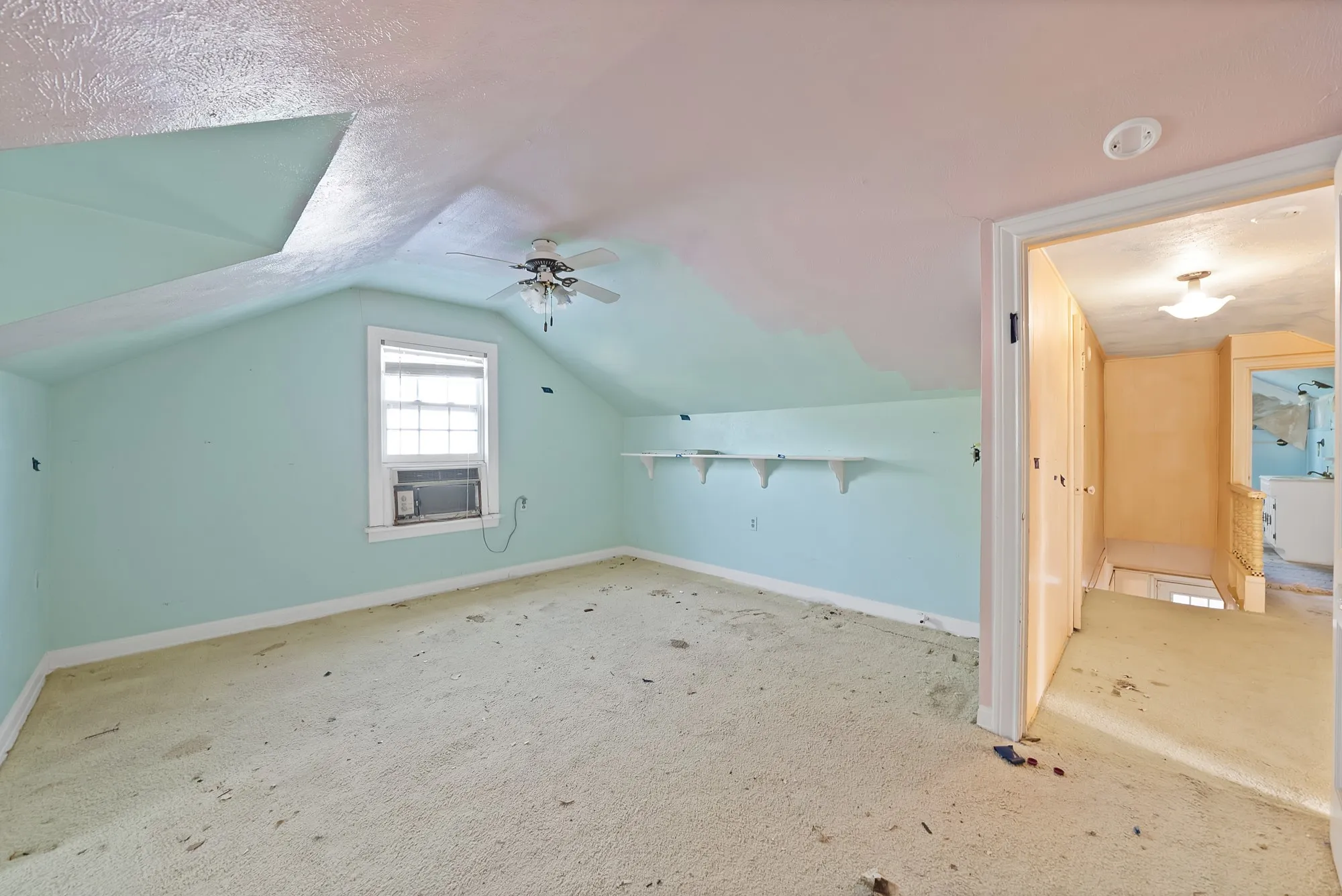 Sloped ceilings, ceiling-mounted fan, window, wall-mounted shelving, and carpeted flooring