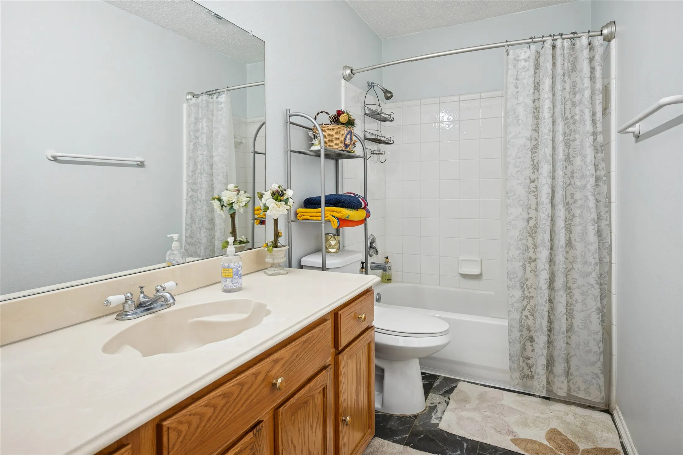 Bathroom featuring a wood-finish vanity with a built-in sink, a large wall-mounted mirror, and a full bathtub with tile surround