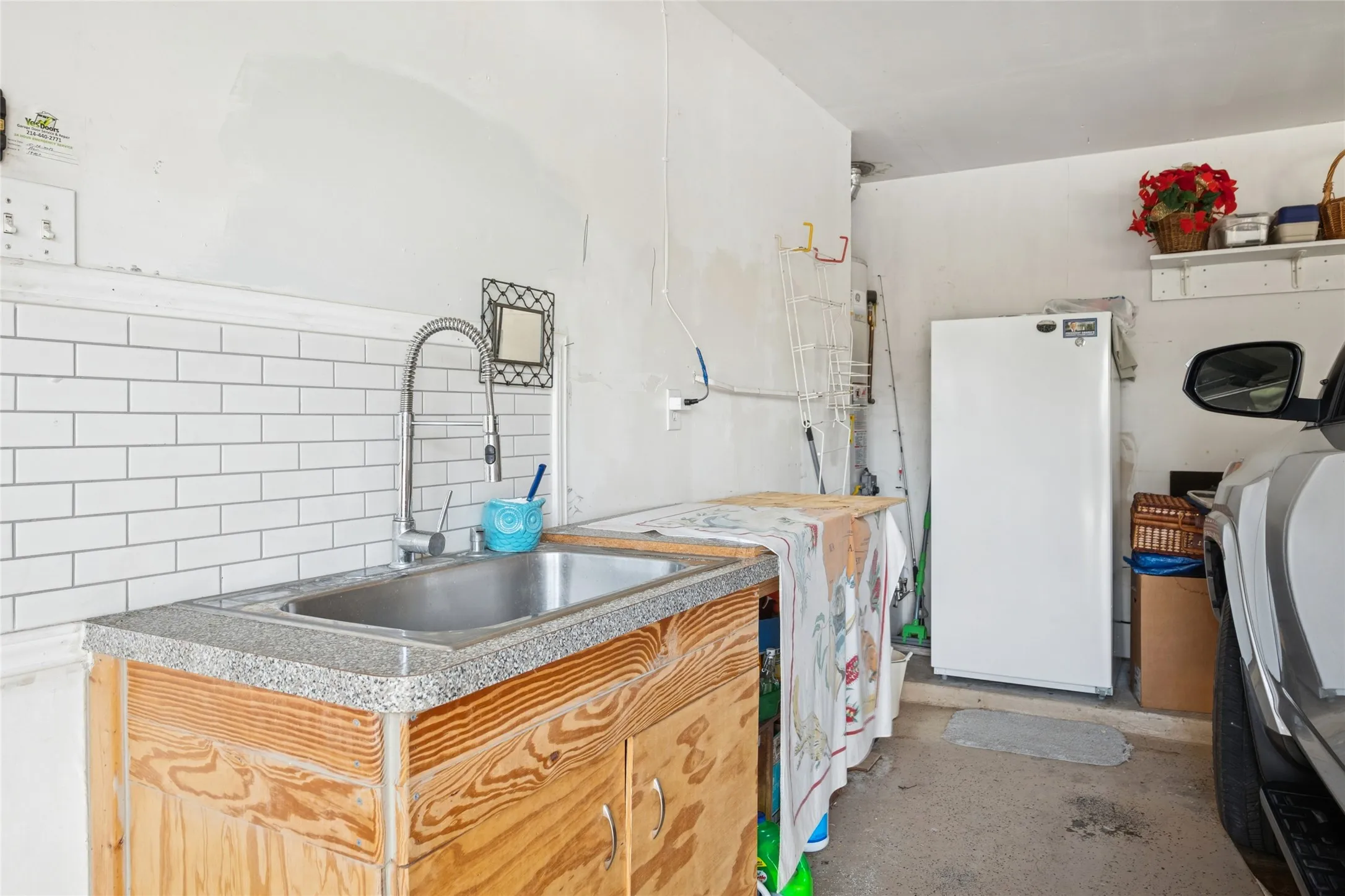 Garage workstation featuring a stainless steel sink, gooseneck faucet, and white backsplash