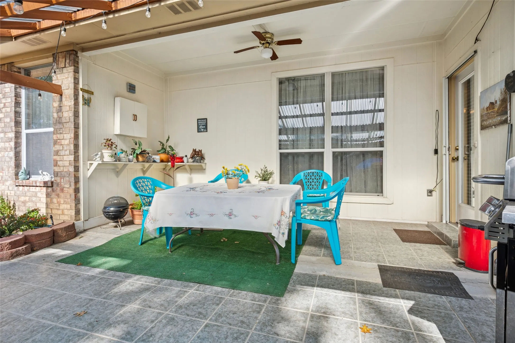 Covered patio featuring a ceiling fan, permanent wall shelving, and a brick accent wall