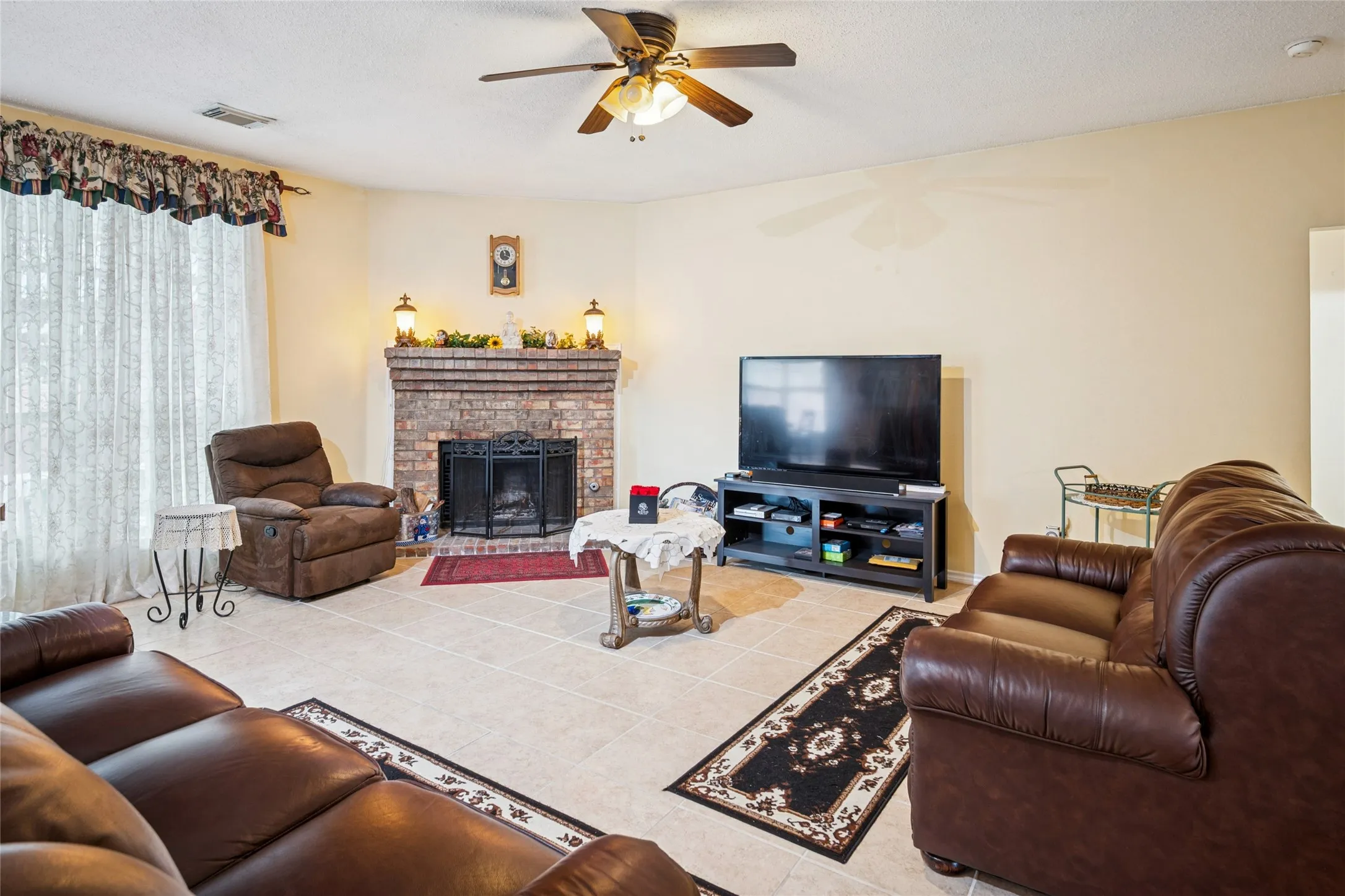 Brick-surround fireplace with hearth, tile flooring, and ceiling fan