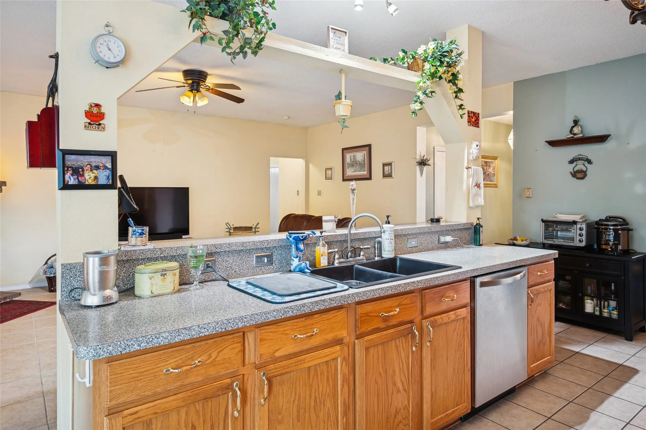 Kitchen featuring wood-finish cabinetry, a double basin sink, a stainless steel dishwasher, and tiled flooring