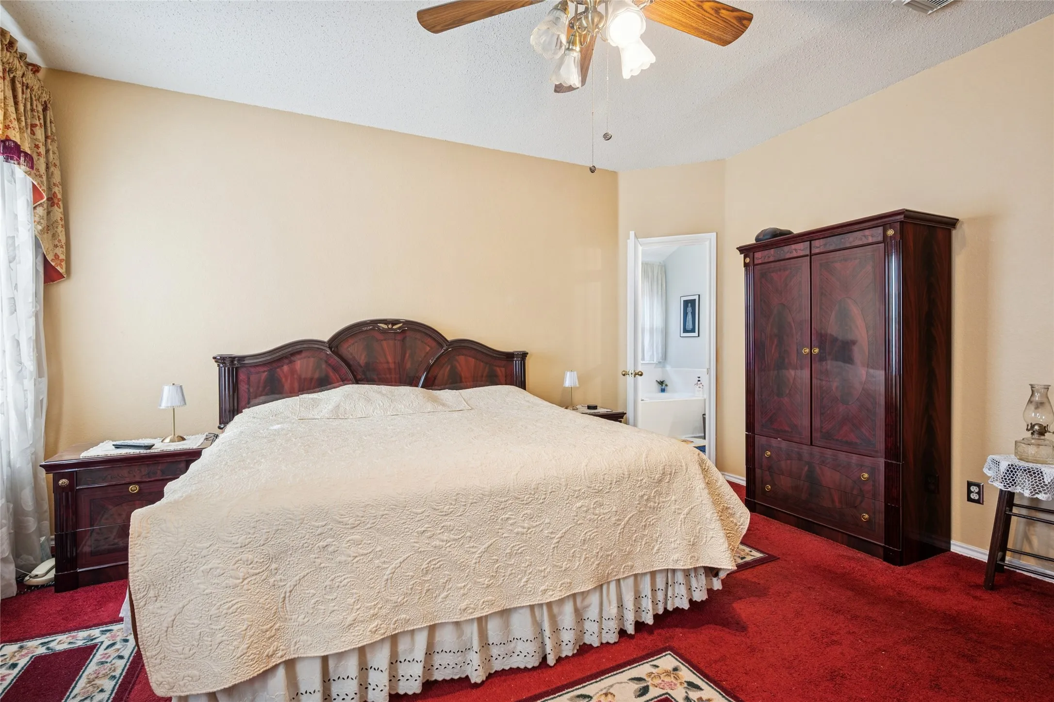 Ceiling fan with light fixture, warm-toned walls, carpeting, and an arched entryway