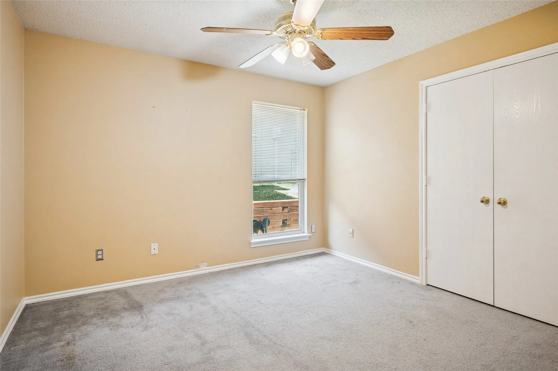 Recessed window with blinds, ceiling fan with light fixture, and double-door closet