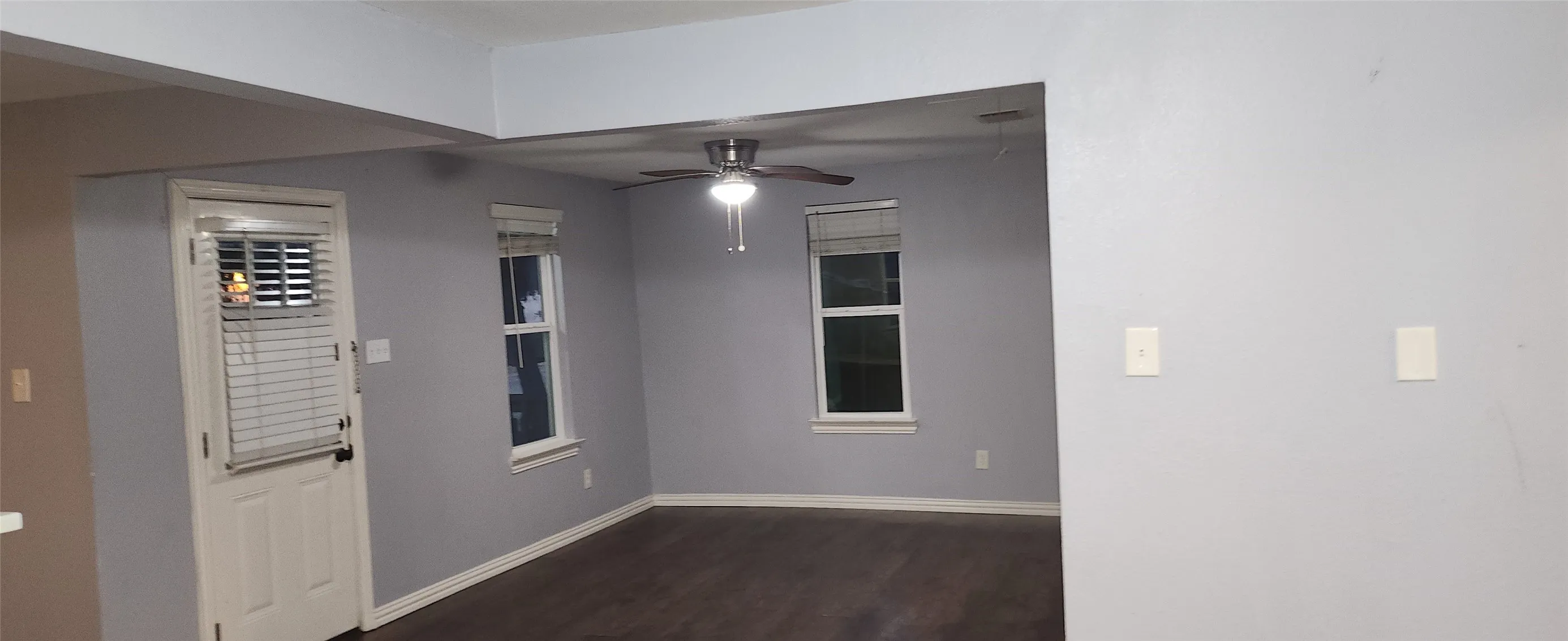 Spacious room featuring wood-finish flooring, light grey painted walls, white trim, and a ceiling fan with integrated lighting