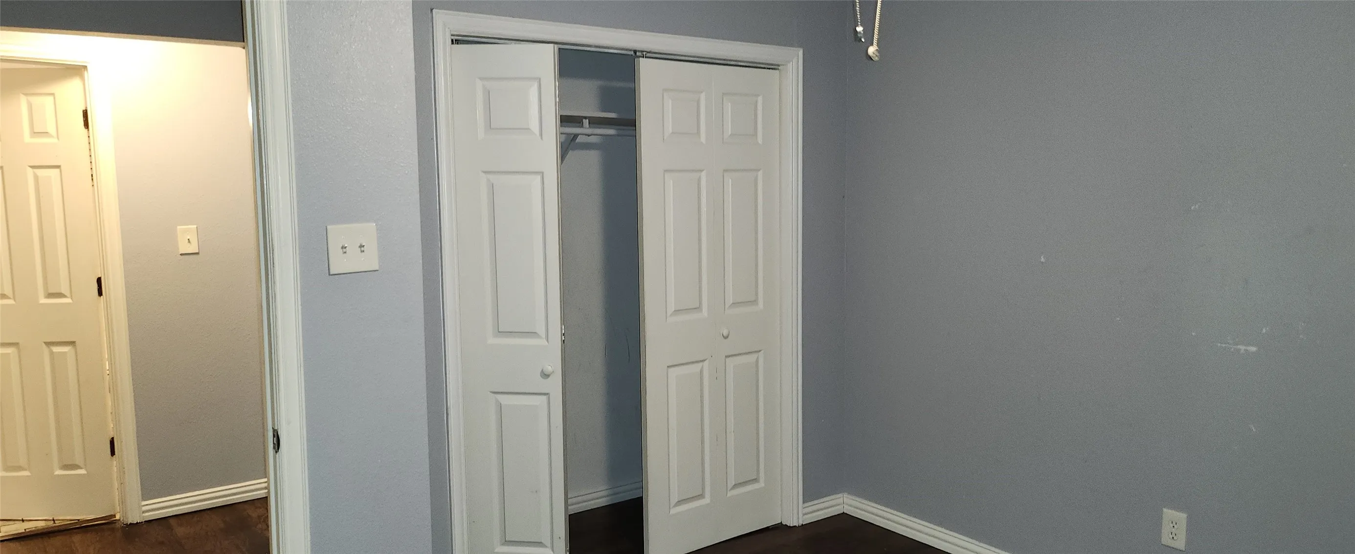 Bi-fold closet doors with an interior hanging rod, dark wood-finish flooring, and light gray wall paint
