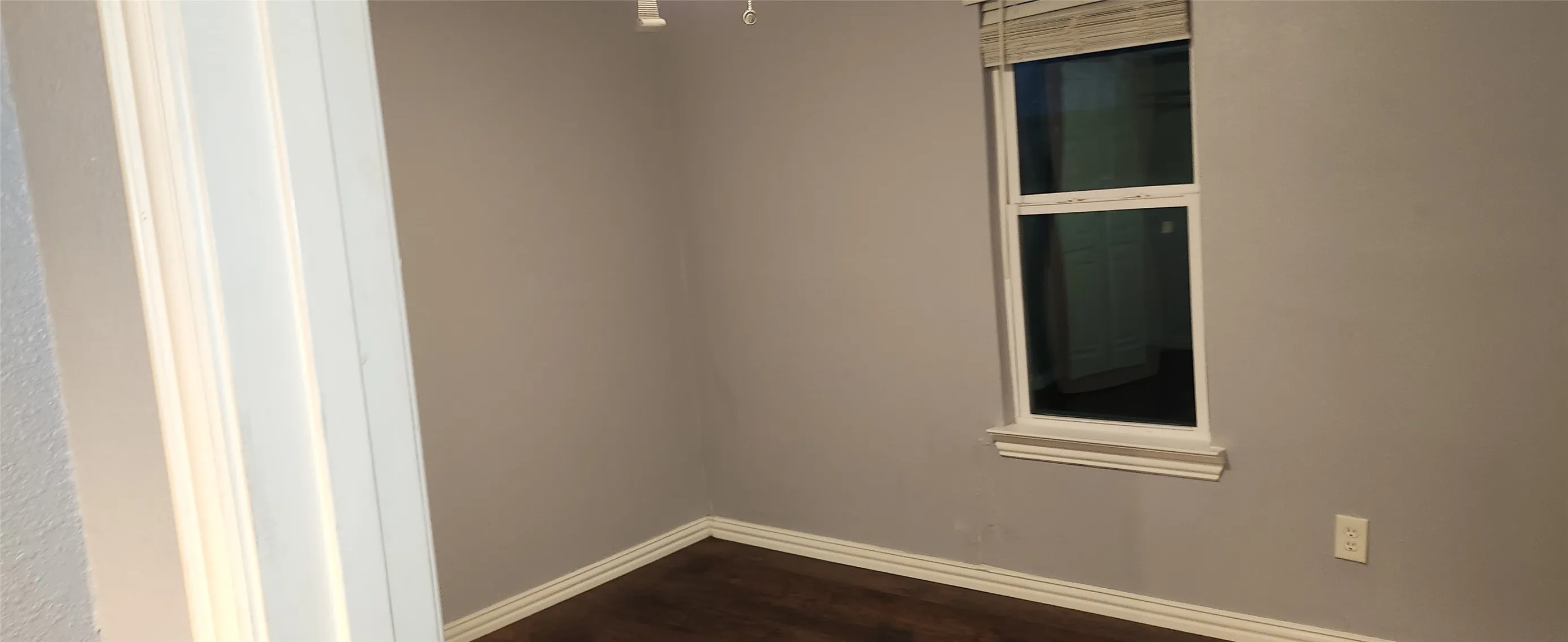 Wood-finish flooring, neutral wall tones, window with blinds, and white trim